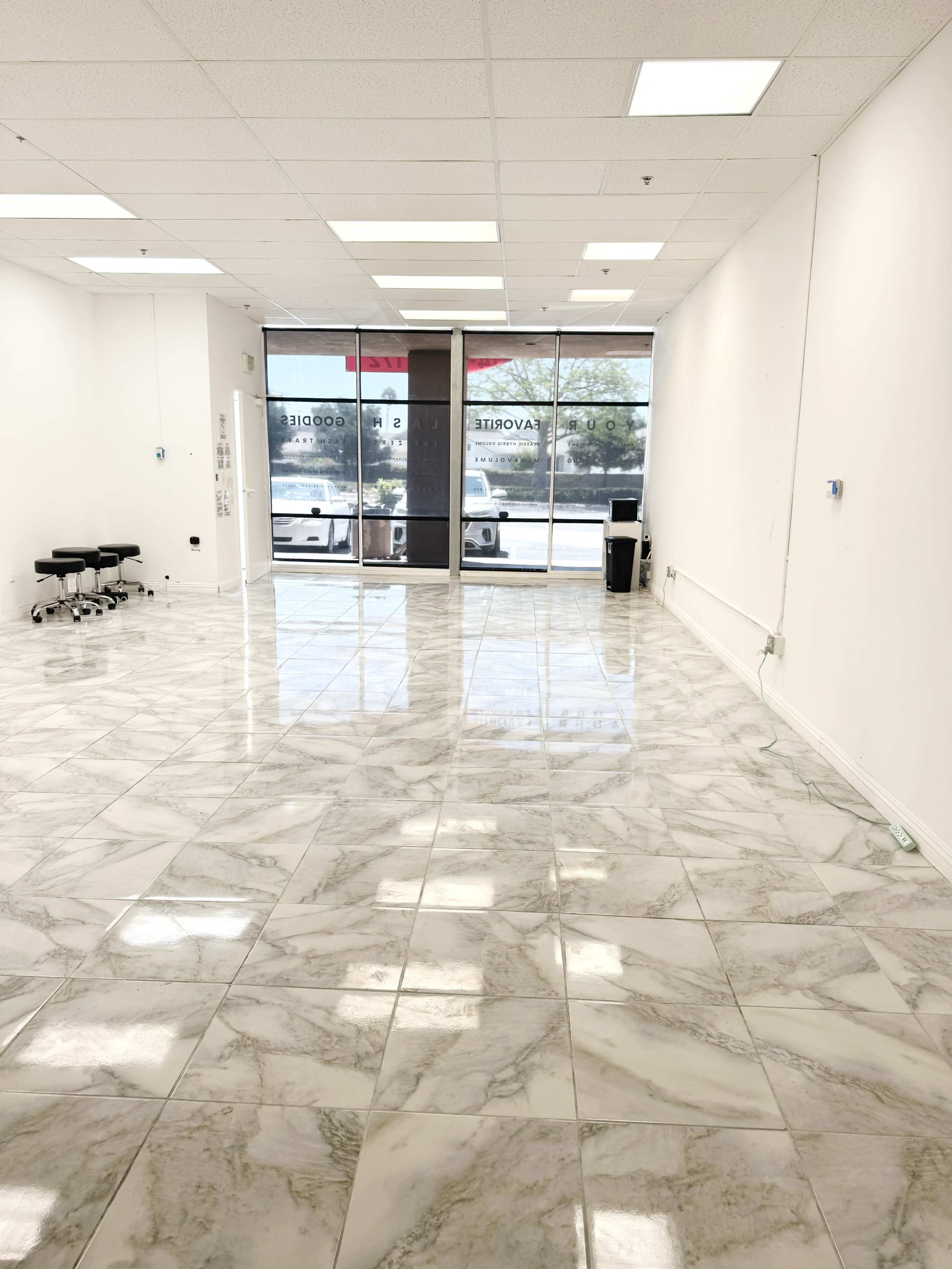 The image shows a spacious, empty room with marble flooring and large windows that allow natural light to enter.