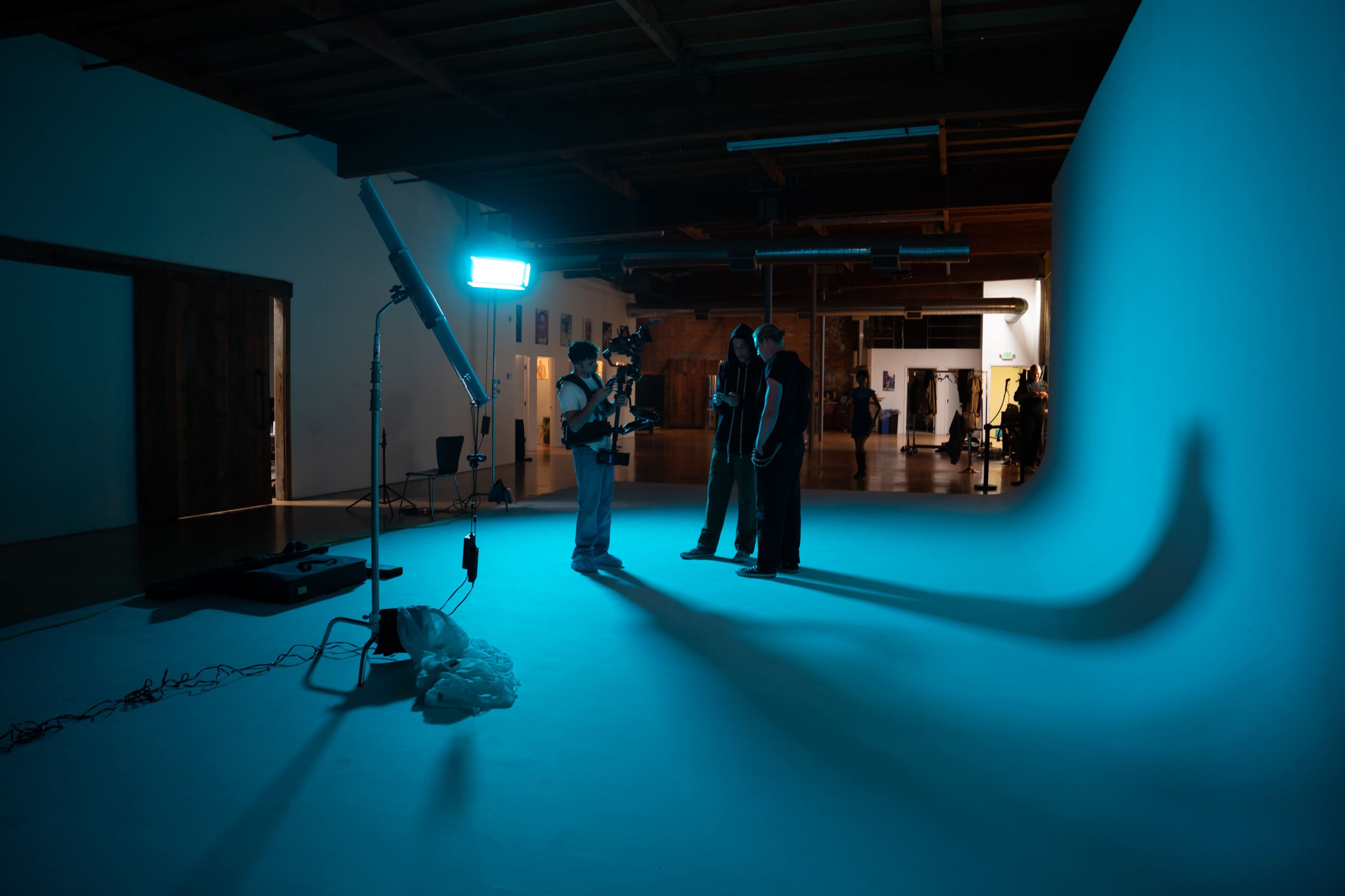 A film crew sets up for a shoot in a spacious studio featuring a blue gradient backdrop and dramatic lighting.