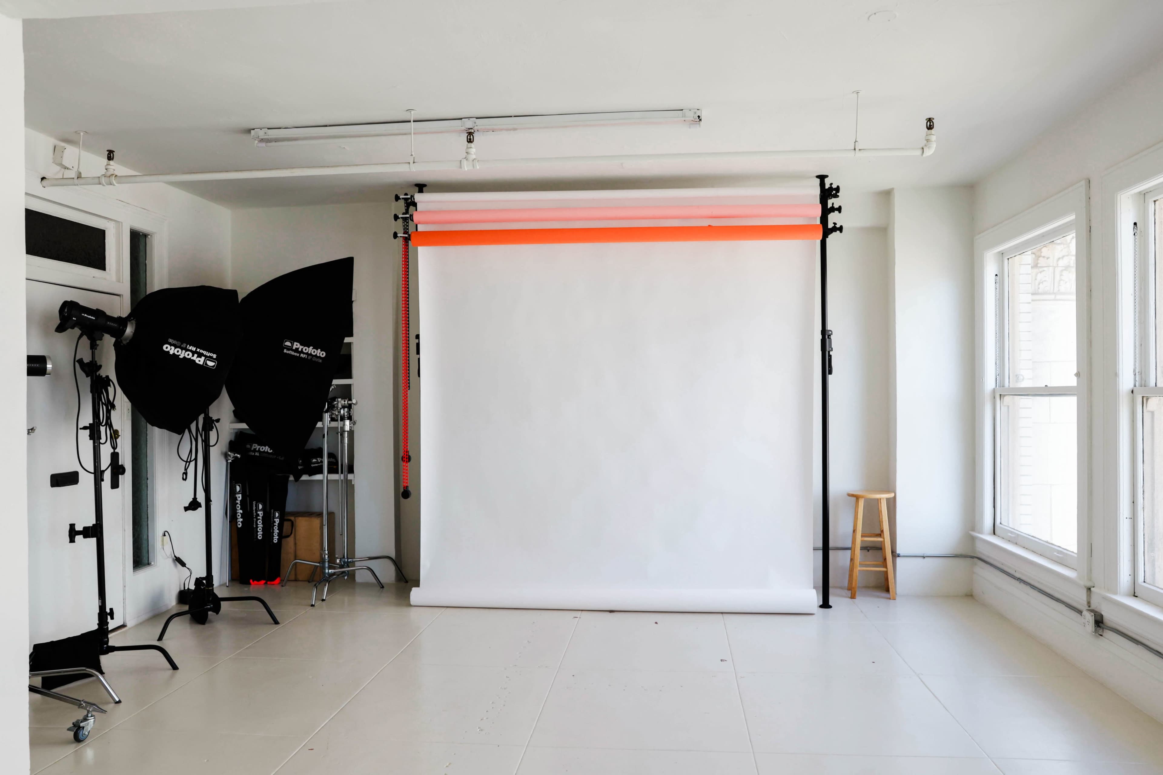A photography studio features a white backdrop mounted on a support system, with softboxes and lighting equipment arranged nearby.