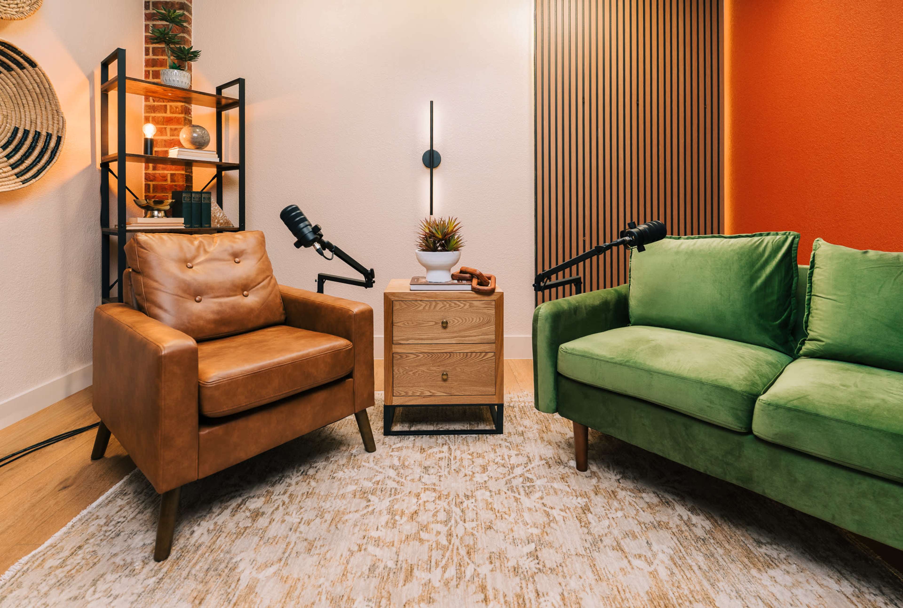 A cozy seating area features a brown leather armchair and a green sofa, flanked by a small wooden side table with a potted plant and microphones on either side.