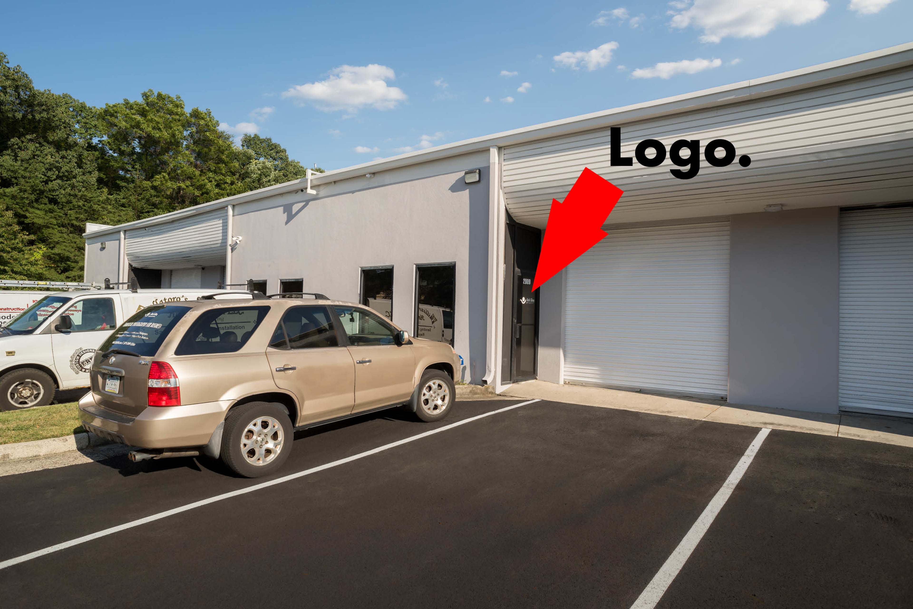 A tan SUV is parked in front of a gray commercial building with loading bay doors and a visible logo on the side.