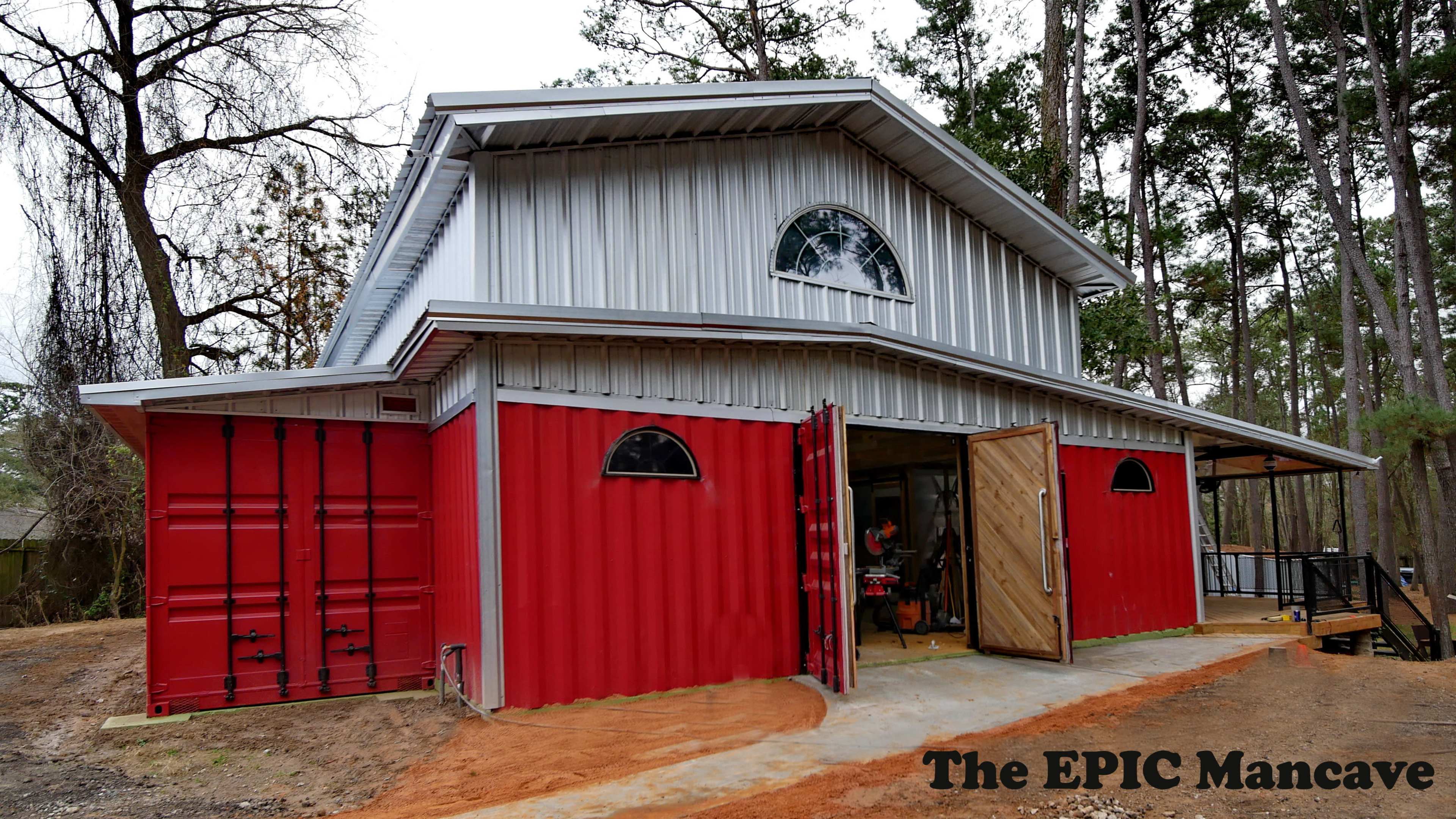 A modern, two-story building constructed with a metal roof and red shipping containers incorporated as walls, surrounded by trees.