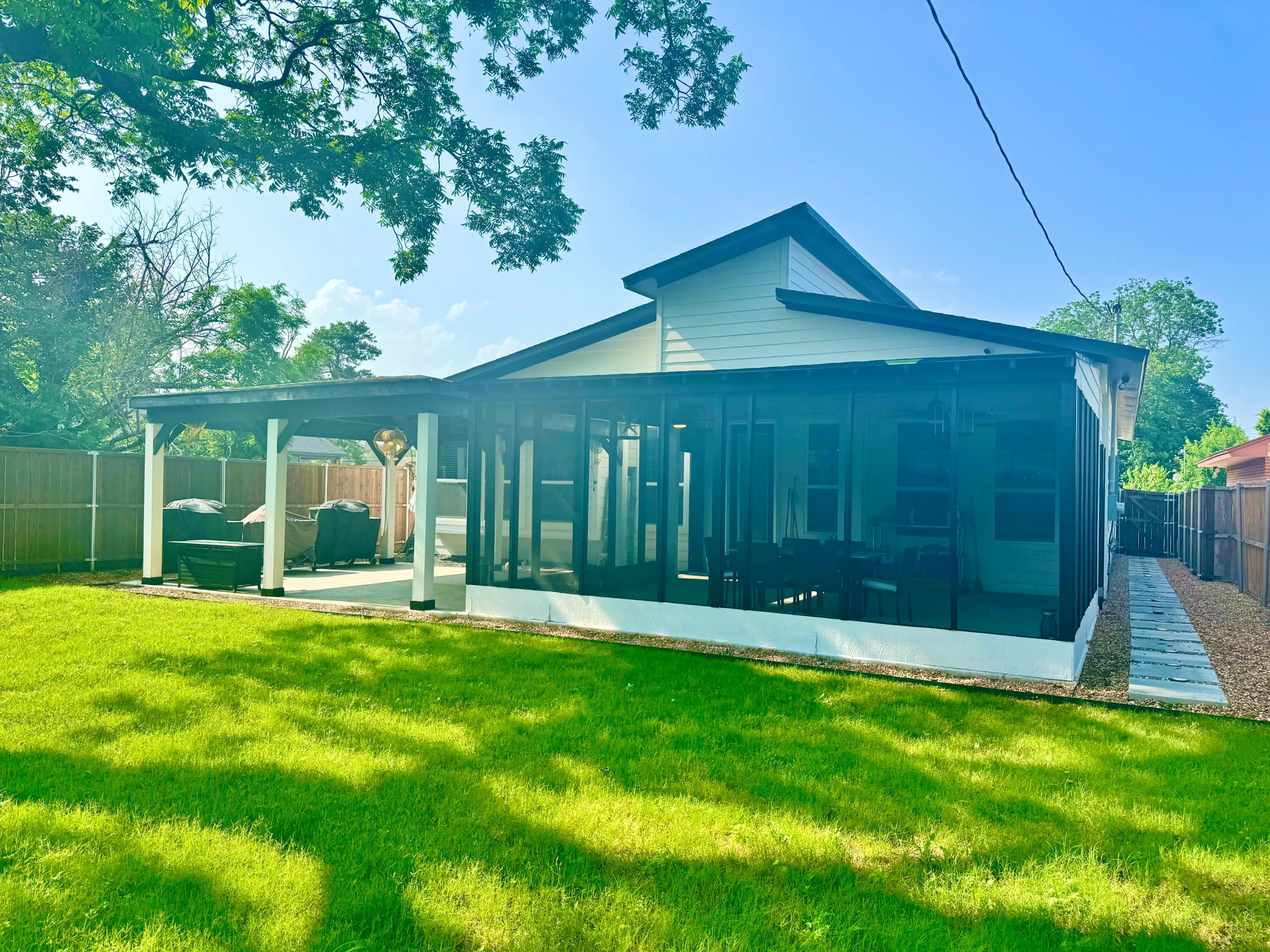 A modern single-story house with a covered patio and a well-maintained lawn, surrounded by a wooden fence.