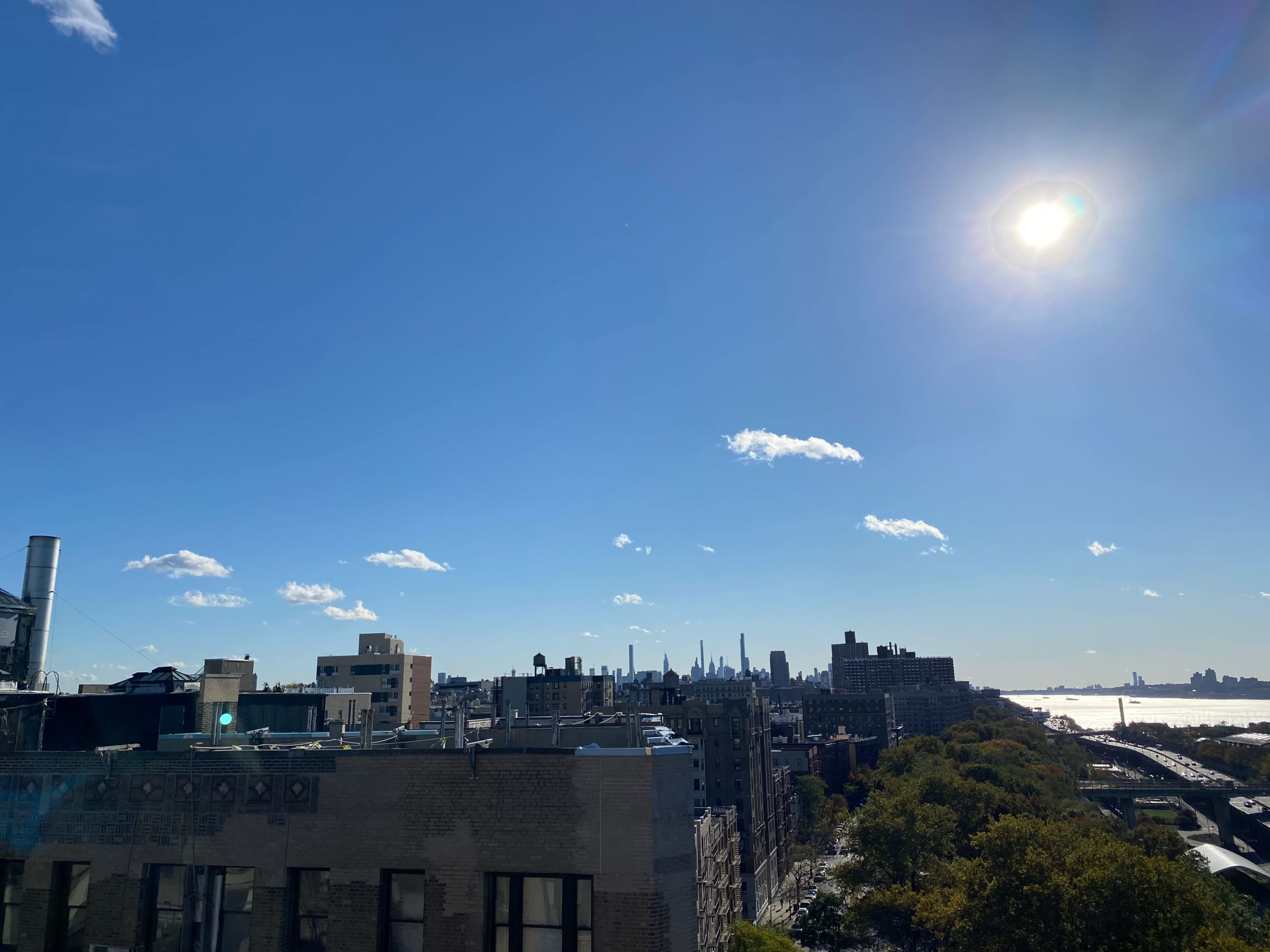The image shows a clear blue sky with a view of a city skyline, including tall buildings, under bright sunlight.
