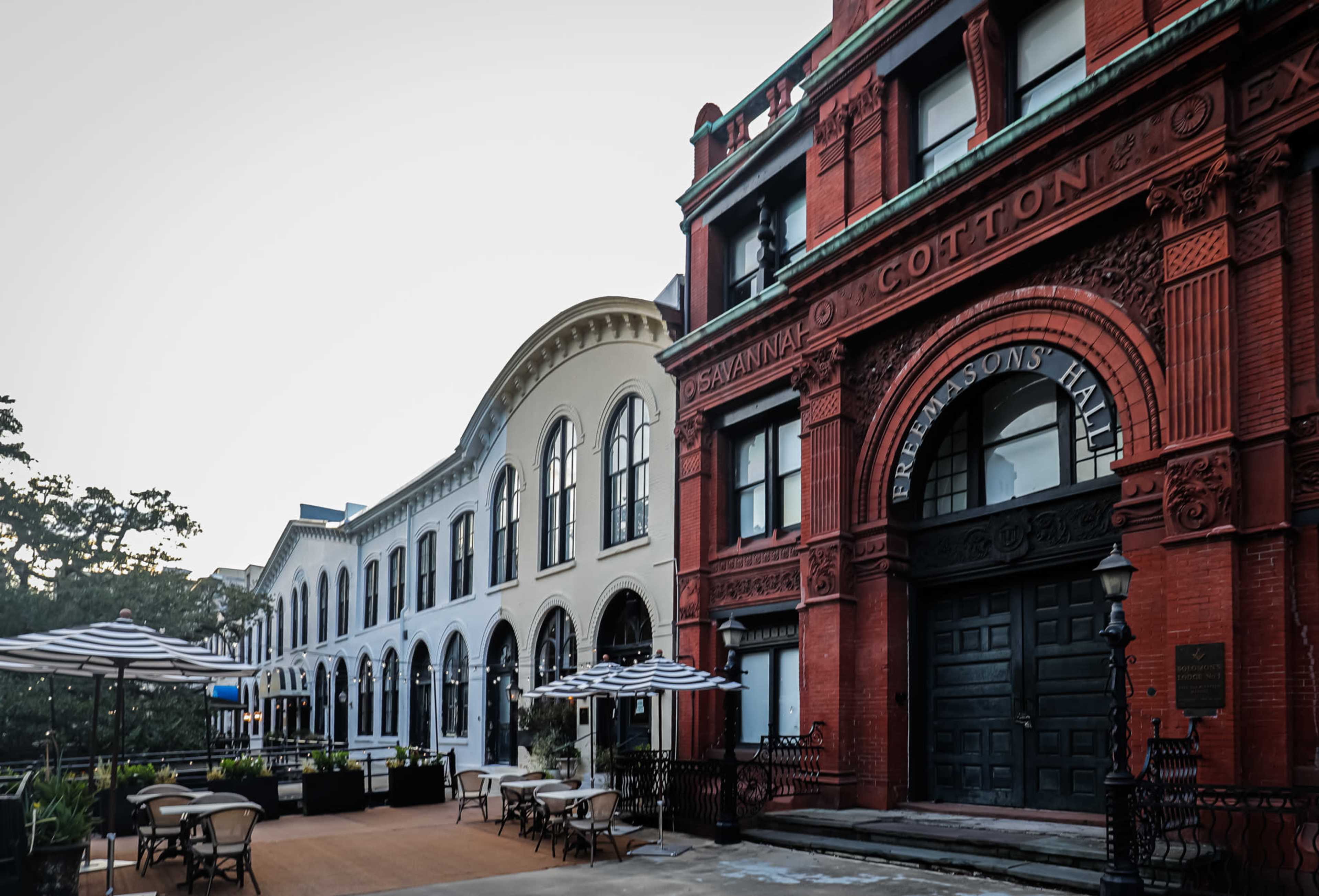 A brick building labeled "Savannah Cotton Exchange" alongside a series of white arched buildings with outdoor seating areas.