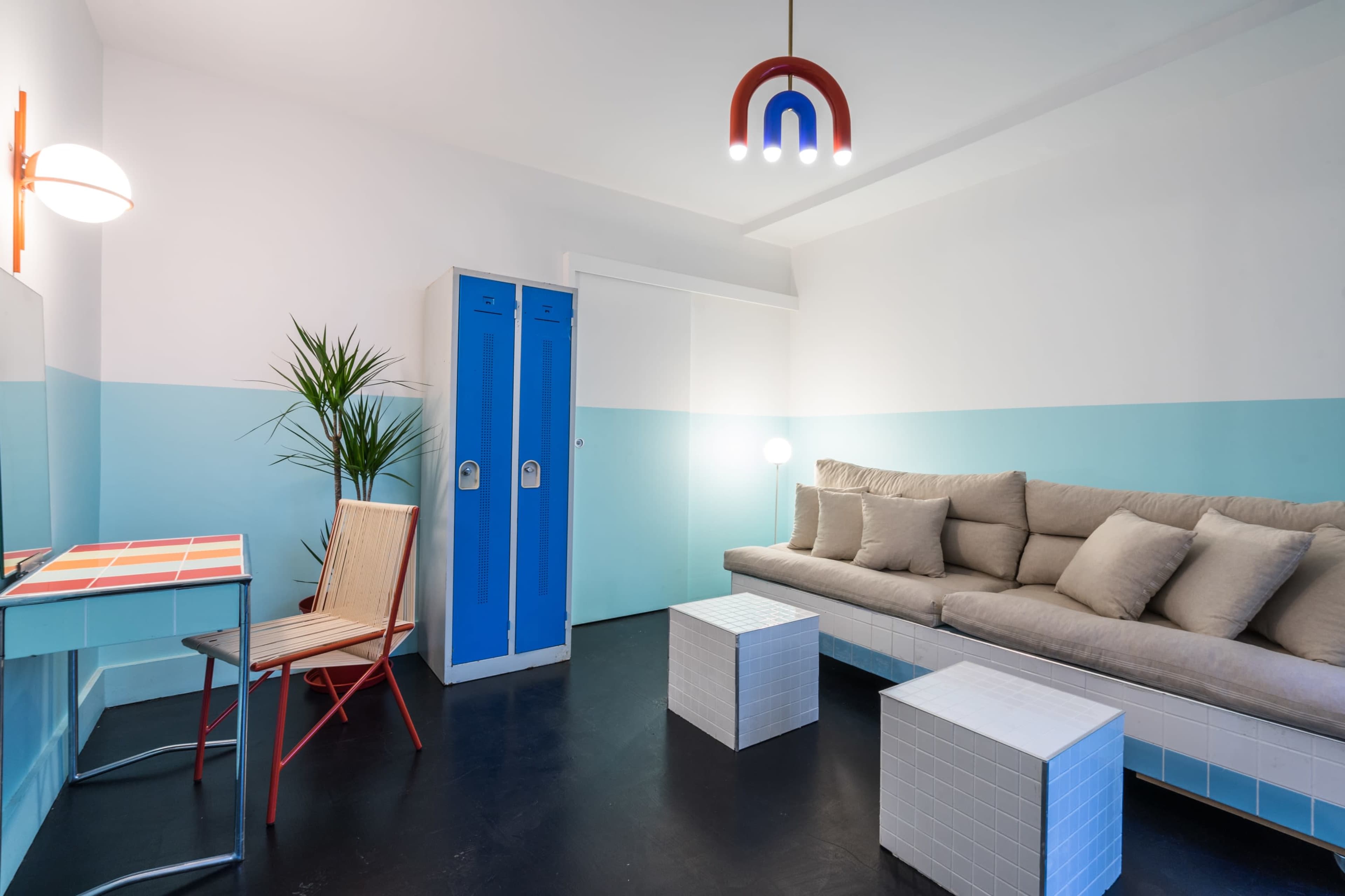 A modern room featuring a light blue and white color scheme, a beige sectional sofa, two white cube tables, a metal chair, and blue lockers.