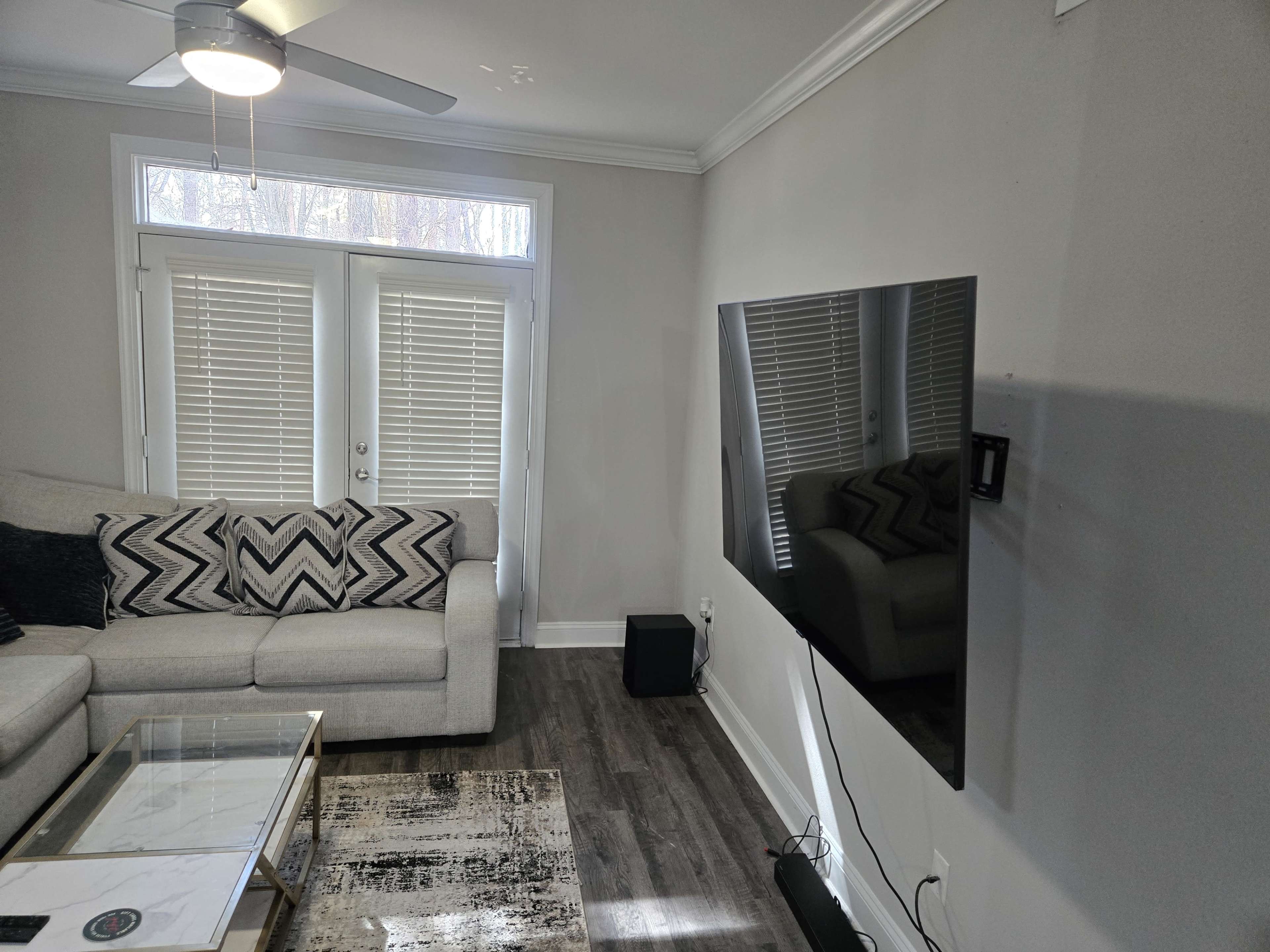 The image shows a living room with a light-colored sofa, a coffee table, and a mounted flat-screen TV on the wall.