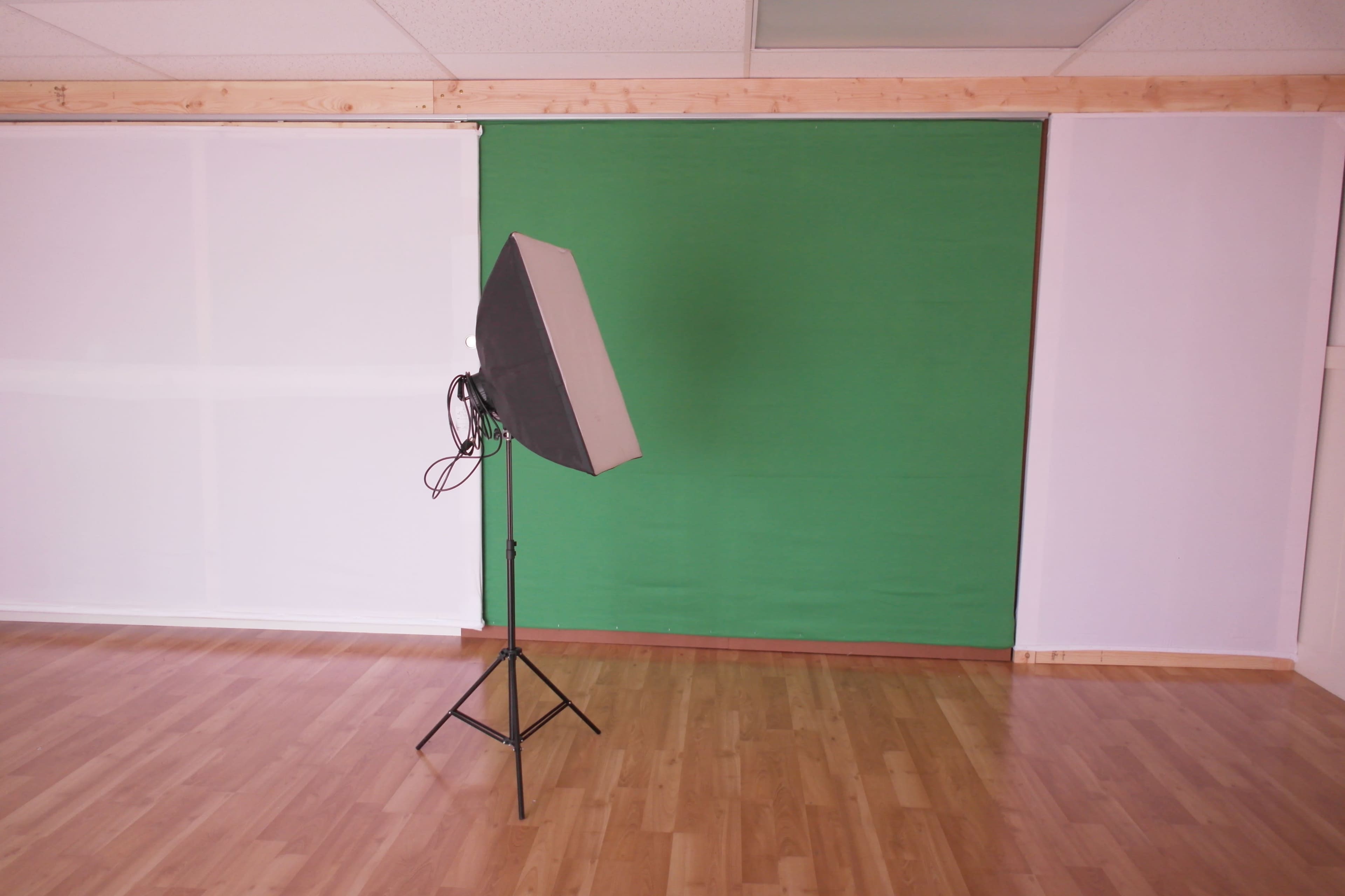 A studio space with a green backdrop and a lighting setup on a stand.