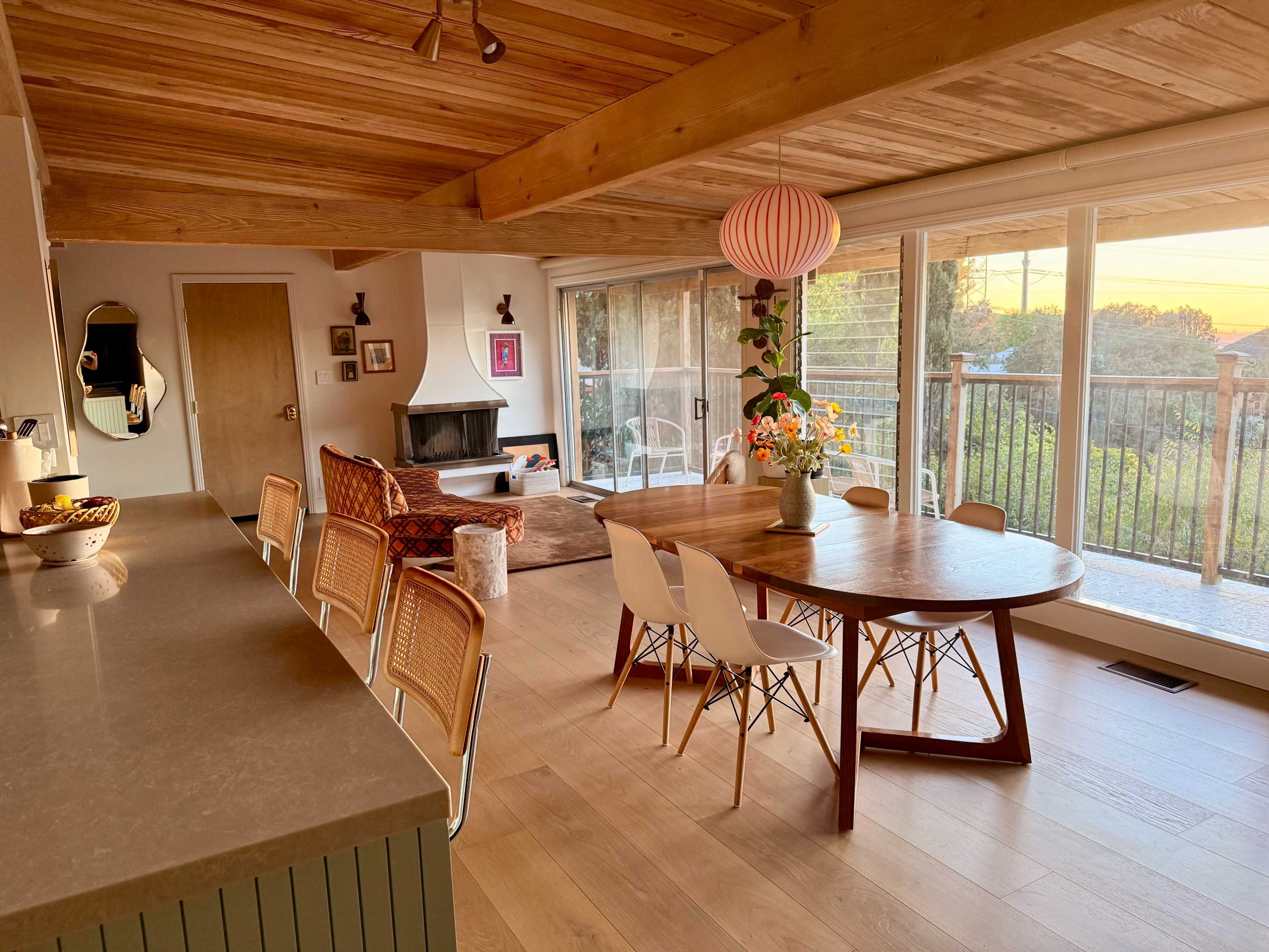 A spacious dining area features a round wooden table surrounded by chairs, with a cozy living space and large windows overlooking a scenic view.