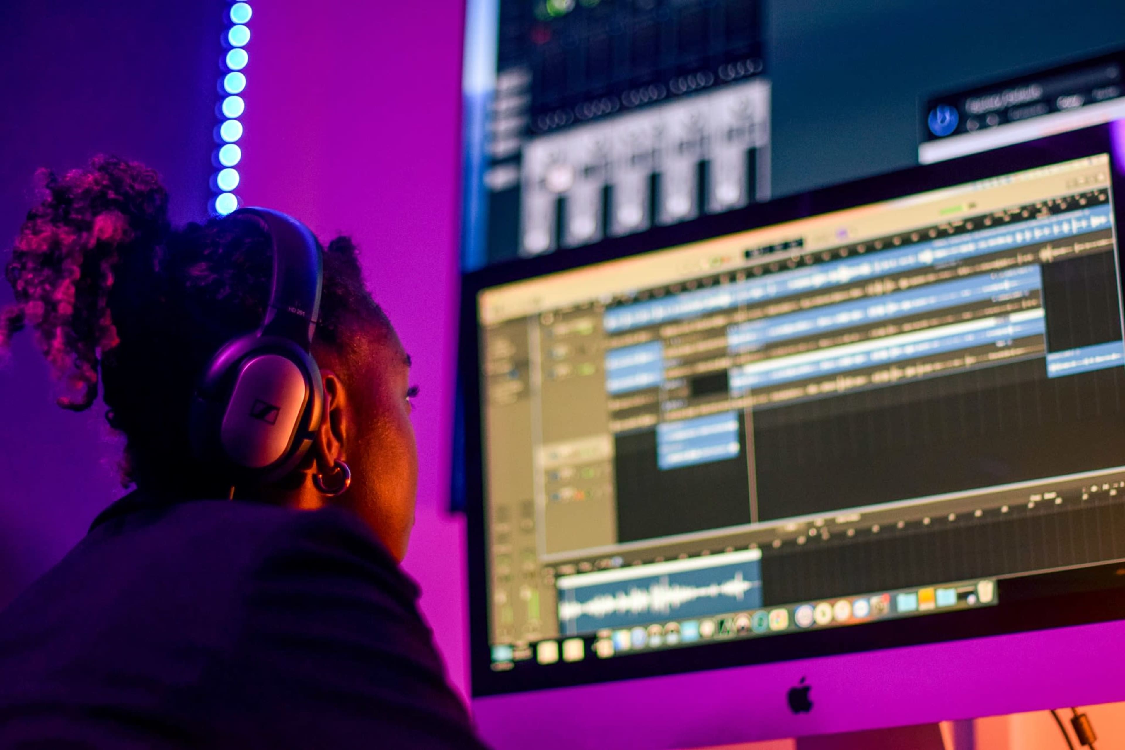 A person wearing headphones is focused on a computer screen displaying music production software.