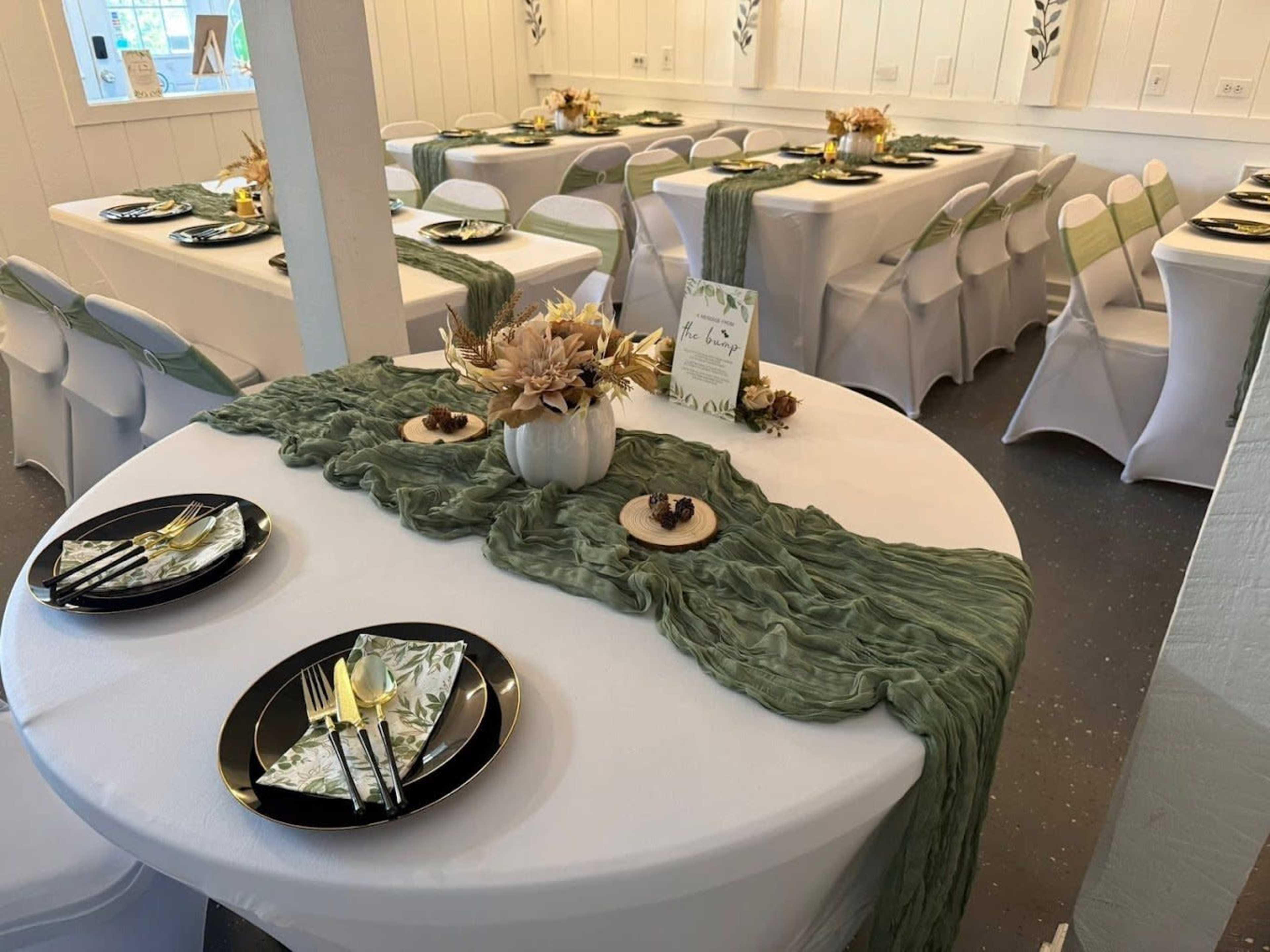 The image shows a dining area with elegantly set tables featuring green table runners, black plates, and decorative centerpieces.