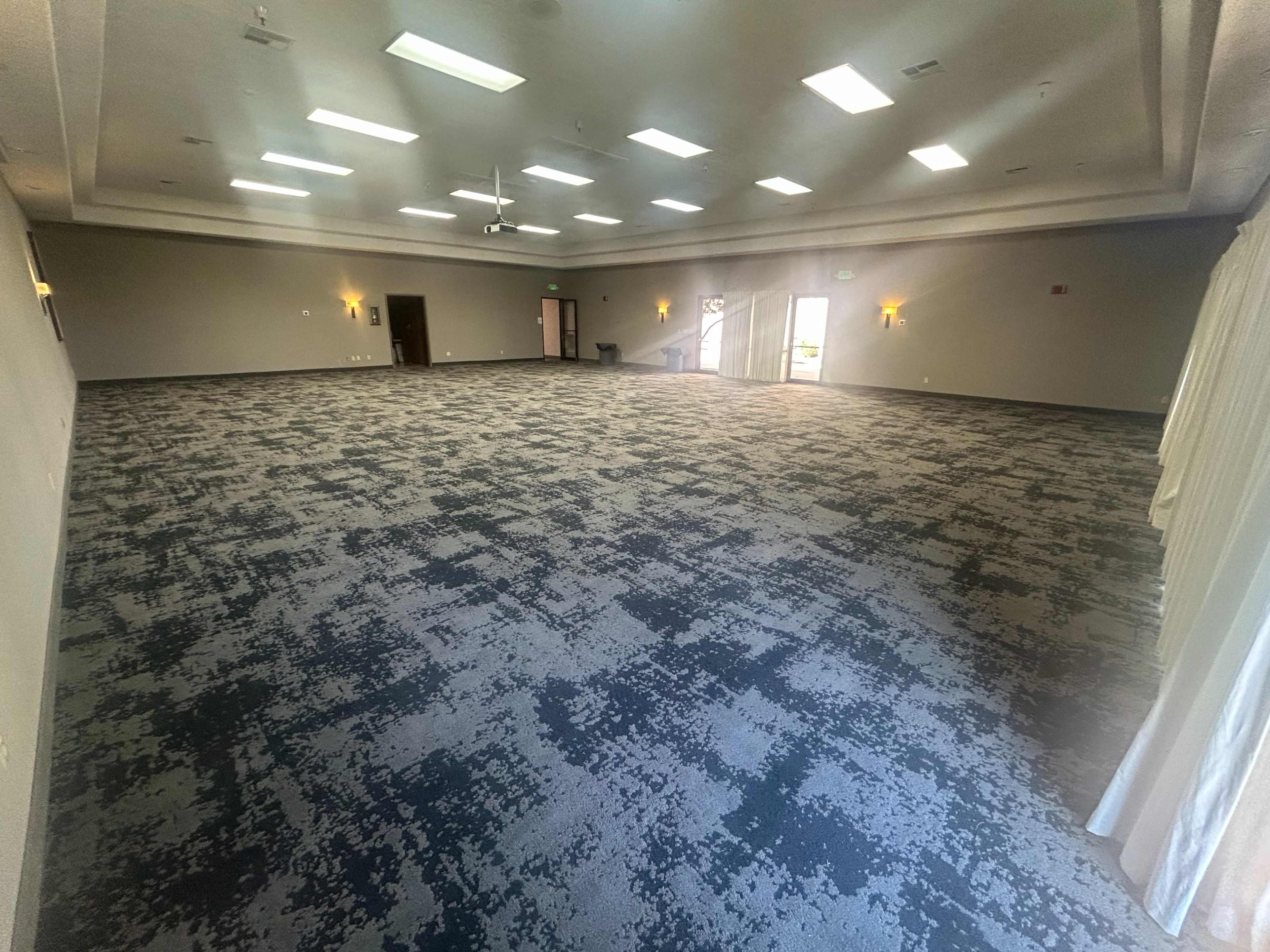 The image shows a spacious, empty room with gray carpet and overhead lights.