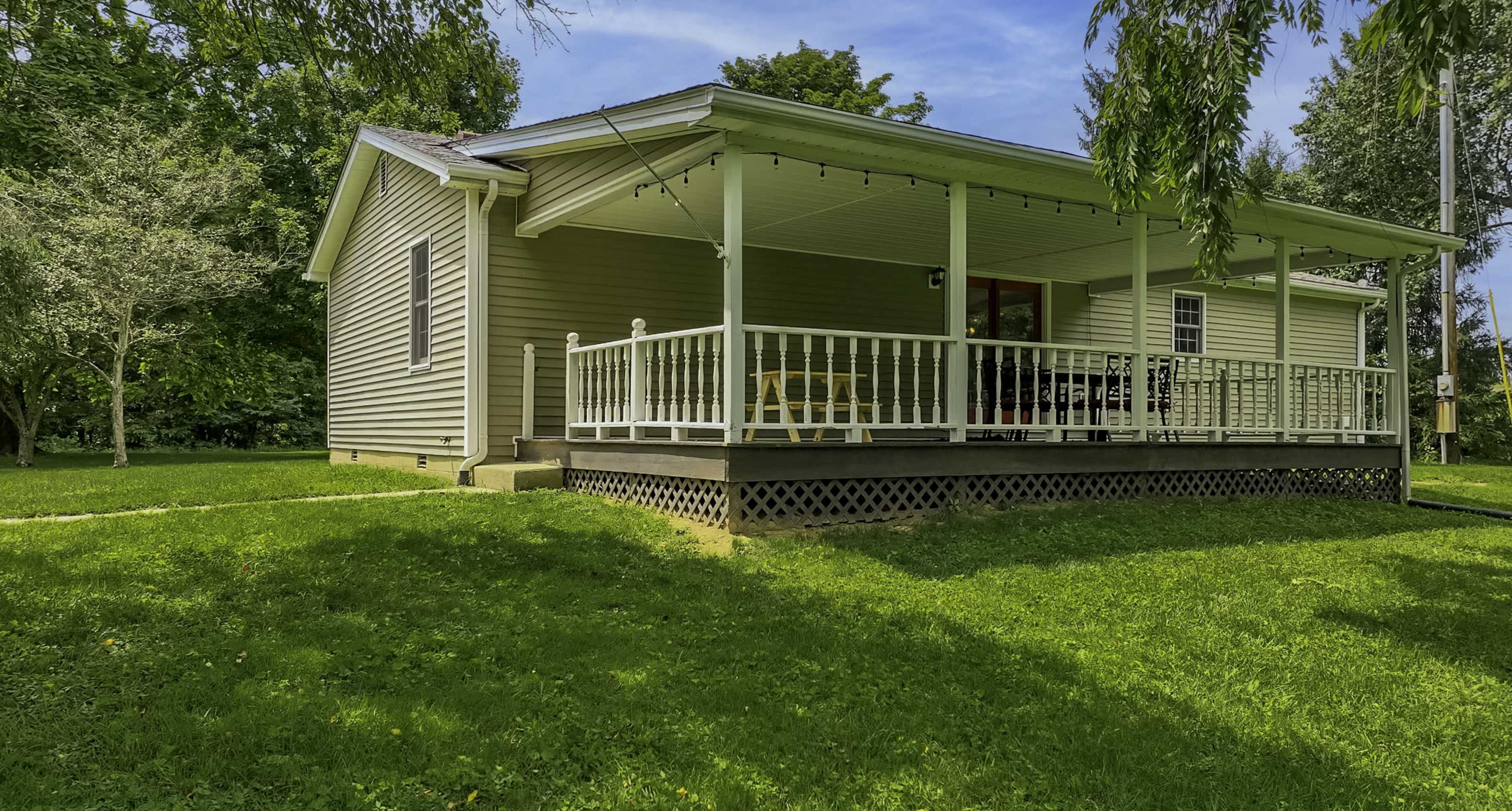 A single-story house with a front porch, surrounded by greenery and grass.