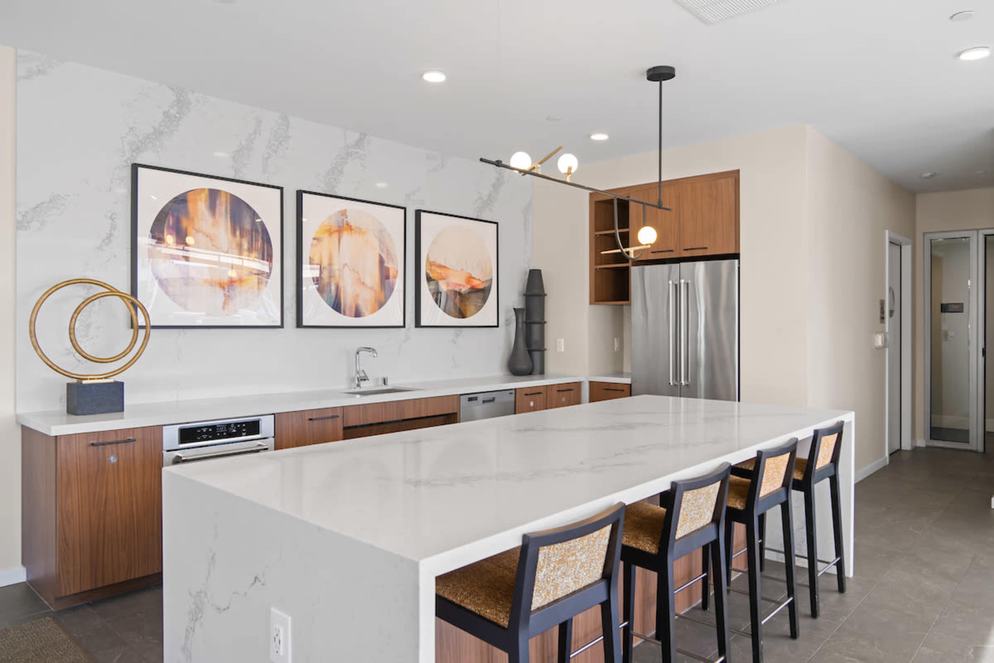 A modern kitchen features a large island with seating, marble countertops, and wooden cabinets along with framed artwork on the wall.