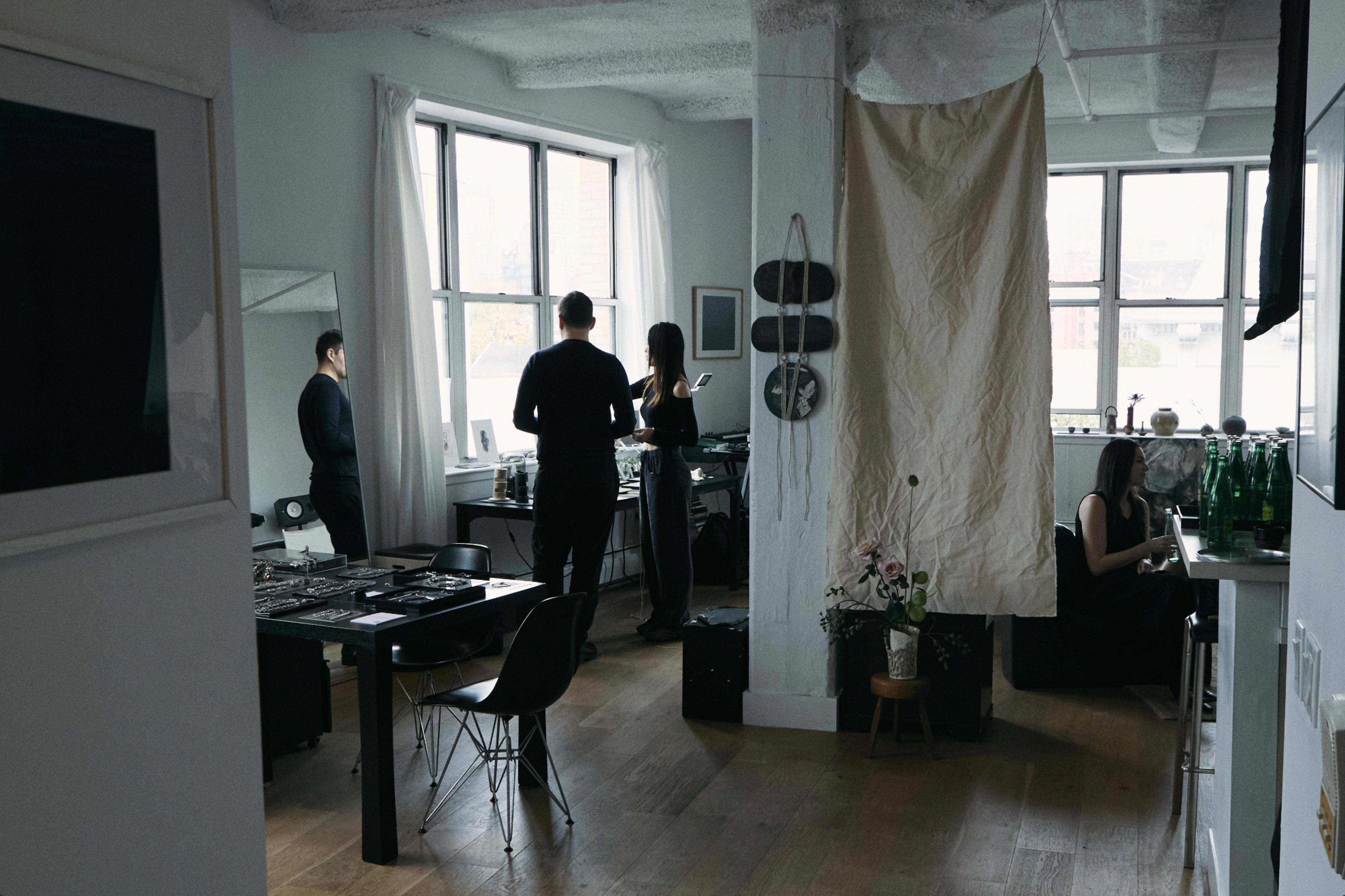 A stylish, modern workspace features people engaged in discussion, surrounded by large windows and minimalist decor.