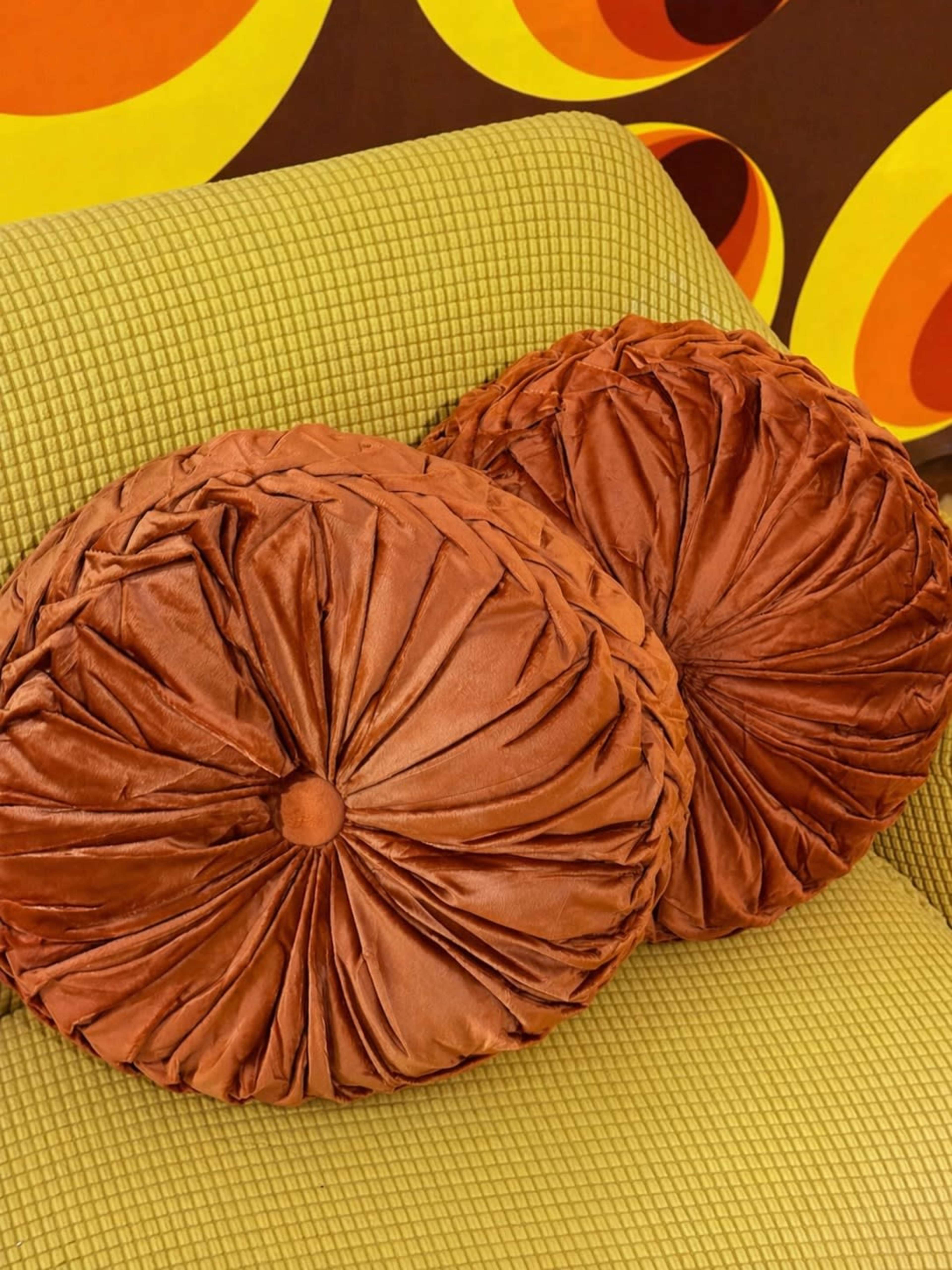 Two round, textured orange pillows are placed on a green patterned couch.