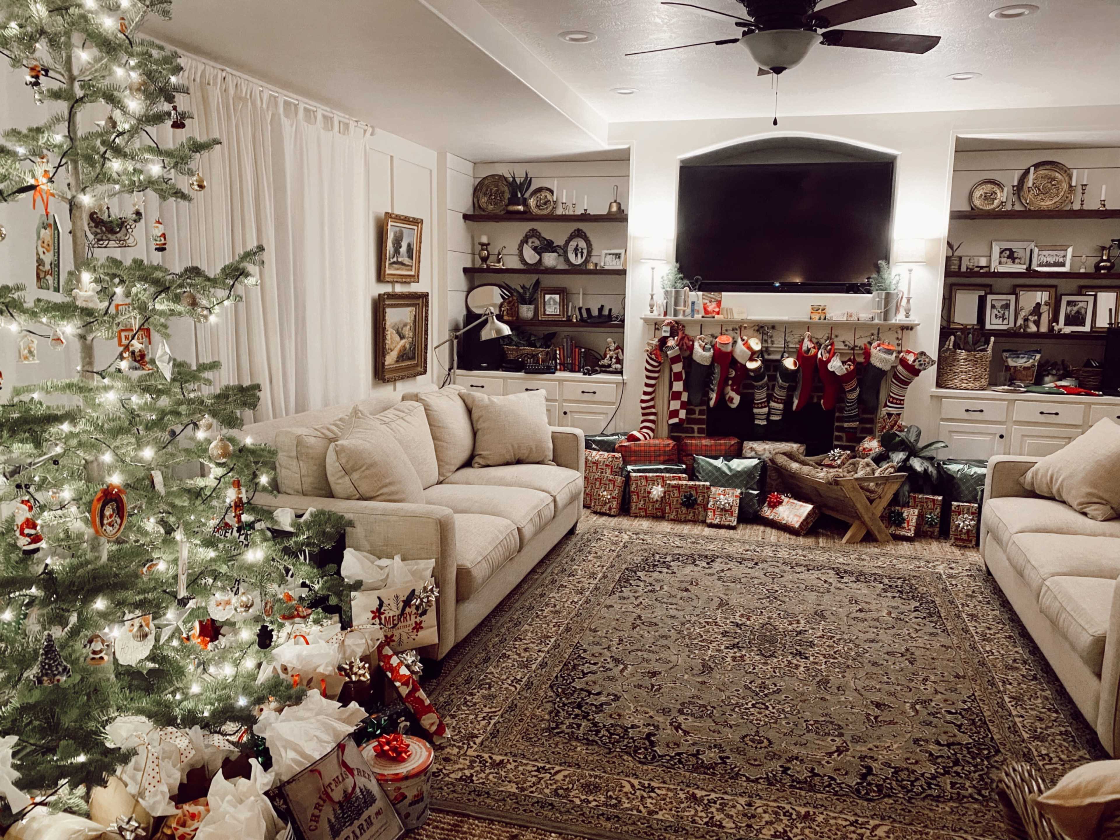 The living room features a decorated Christmas tree, stockings hung over a fireplace, and numerous wrapped gifts on the floor.