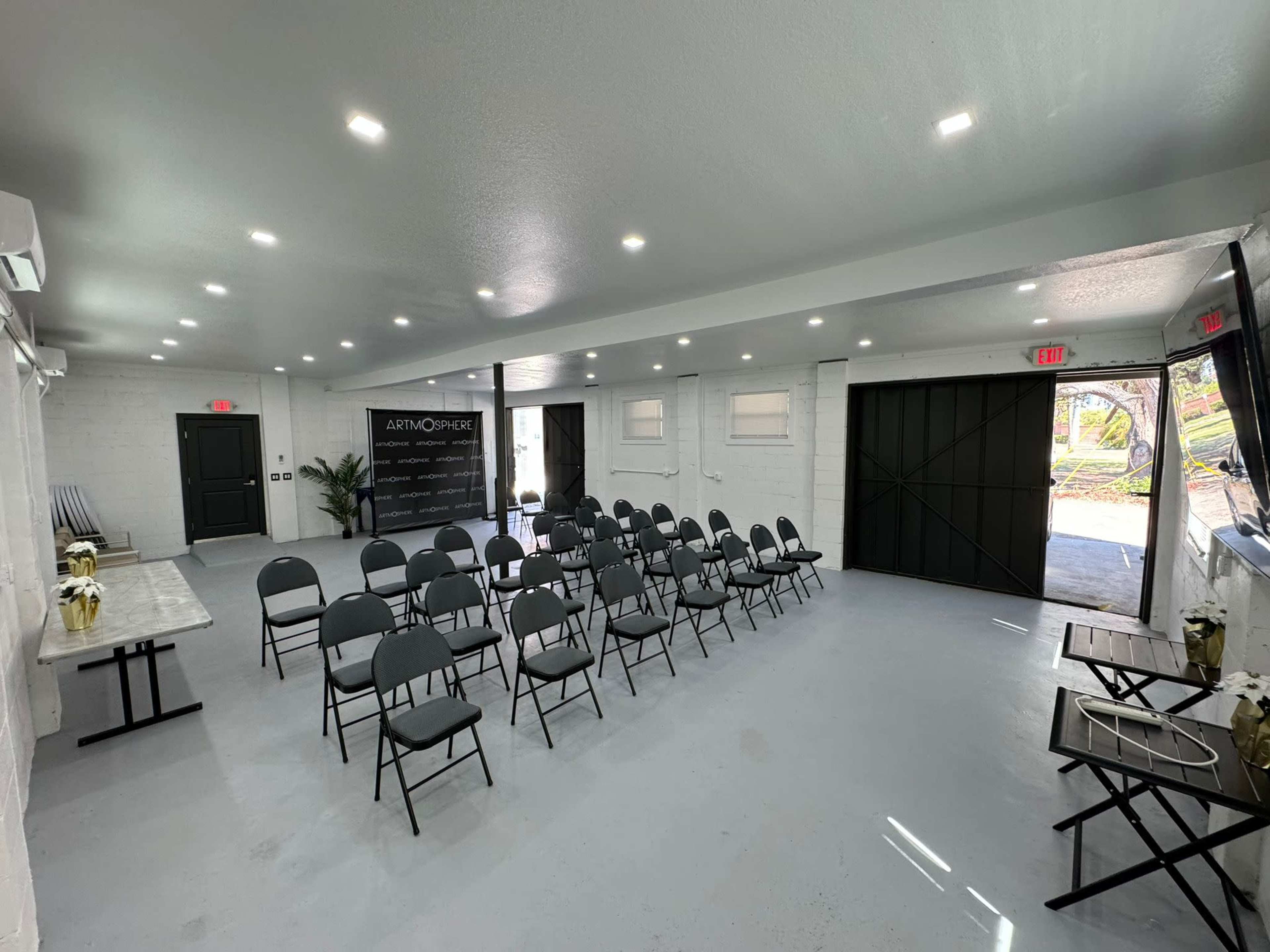 A spacious room set up with rows of chairs facing a presentation area, featuring gray walls and modern lighting fixtures.