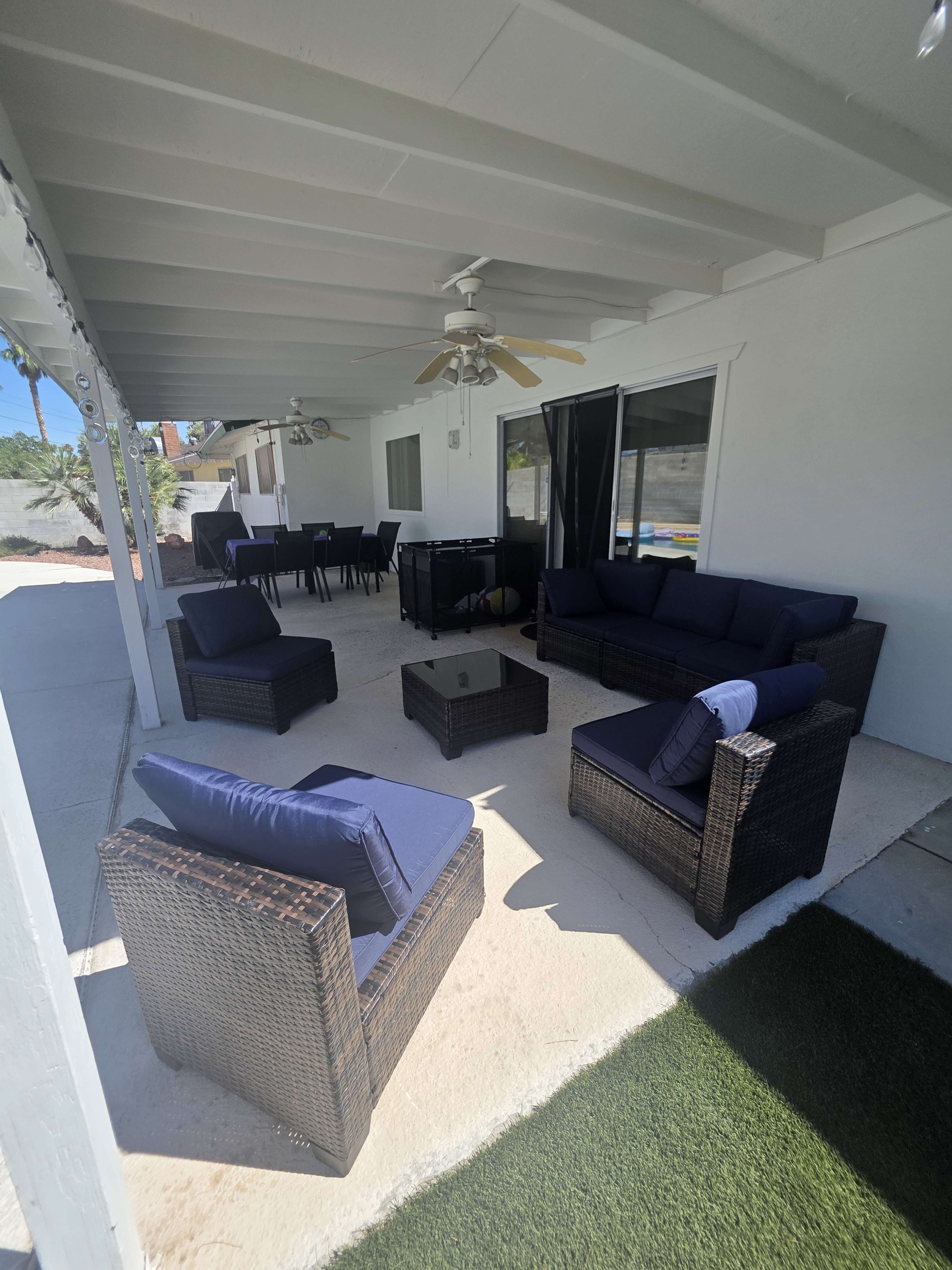 A covered outdoor seating area with wicker furniture and a glass coffee table is arranged on a concrete surface.