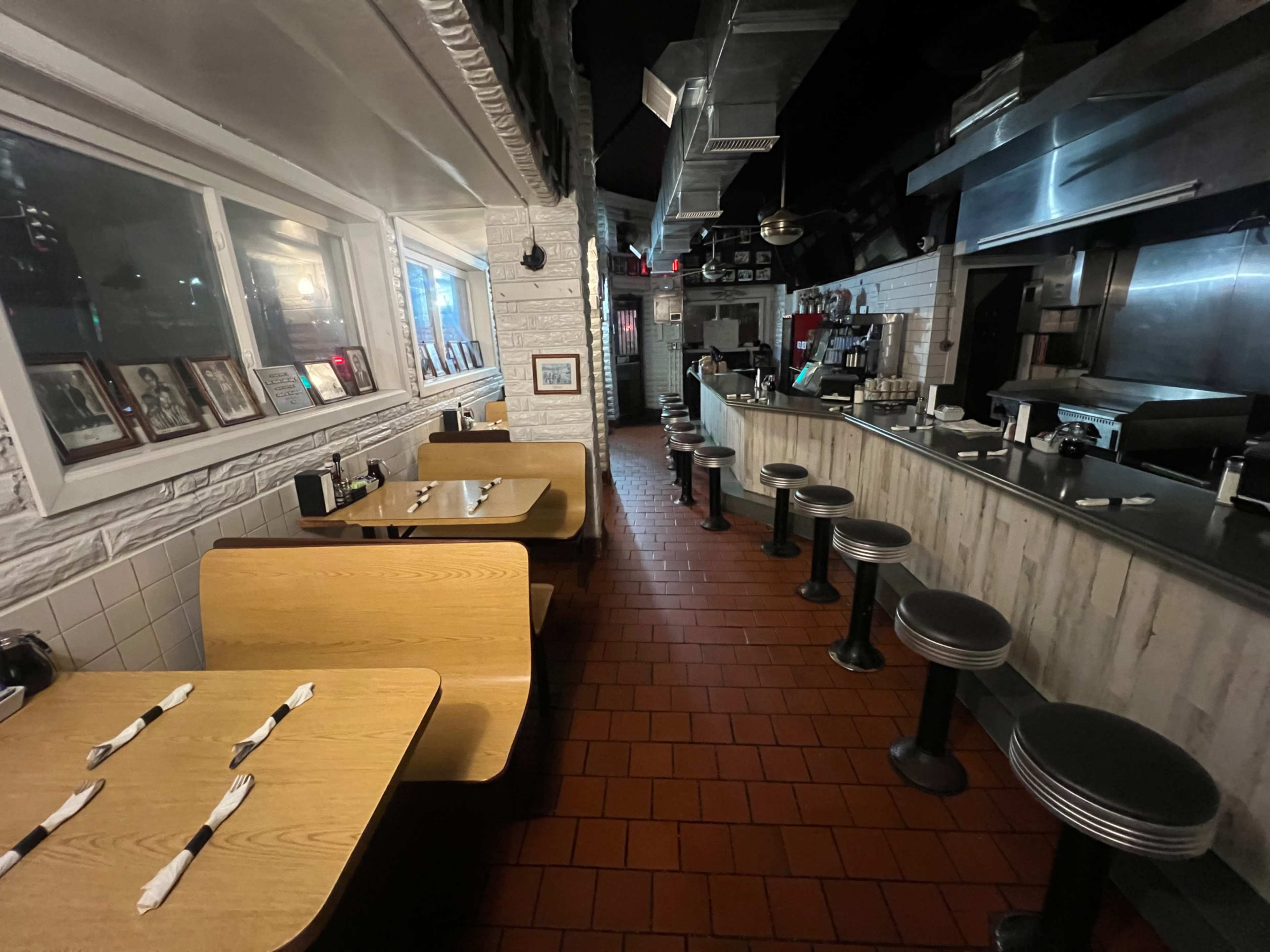 The image shows an empty diner with wooden booths and stainless steel barstools along a counter, illuminated by soft overhead lighting.