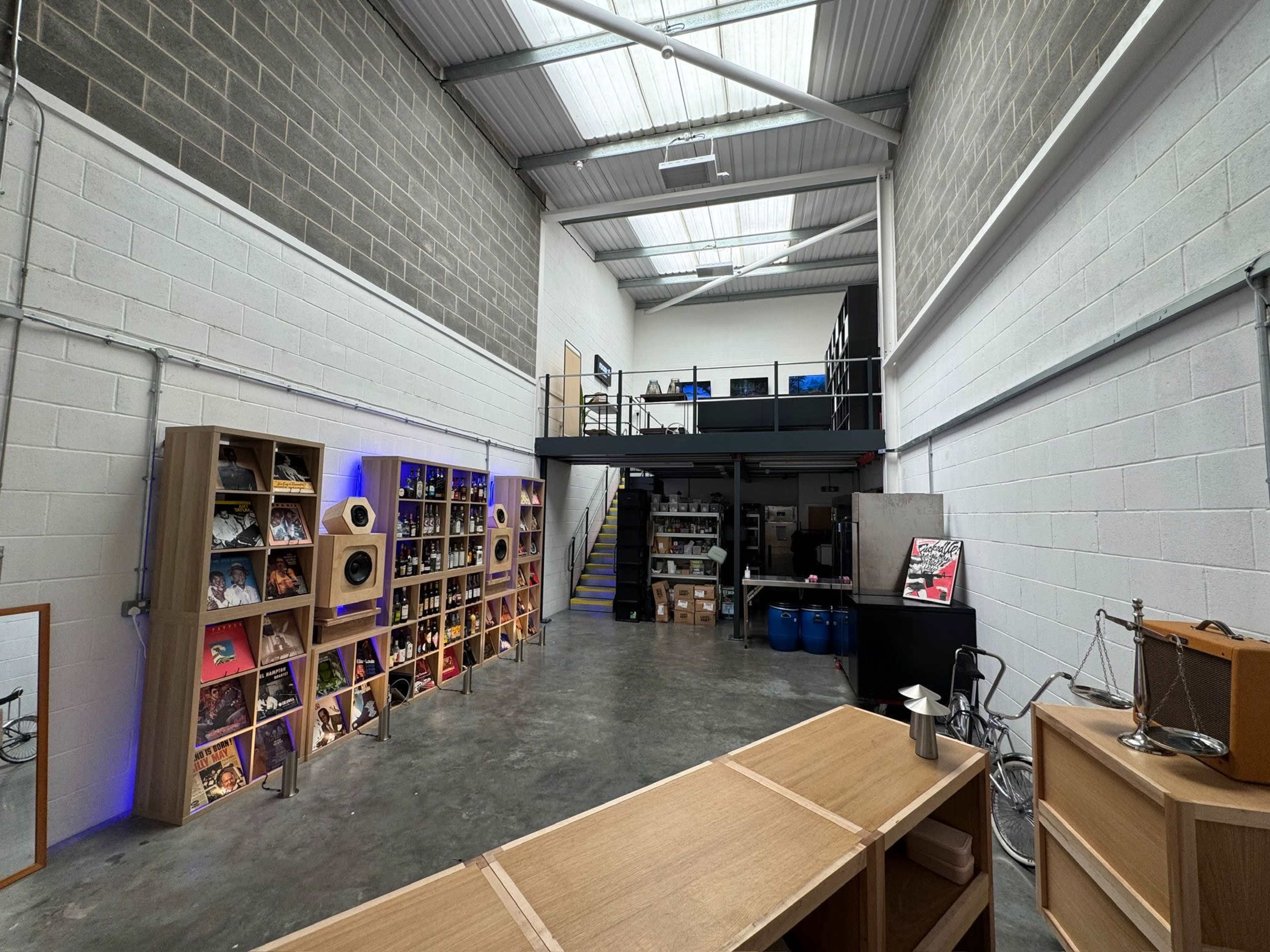 The image shows a spacious industrial-style interior featuring a two-level setup with shelves displaying records, a staircase, and various storage areas.