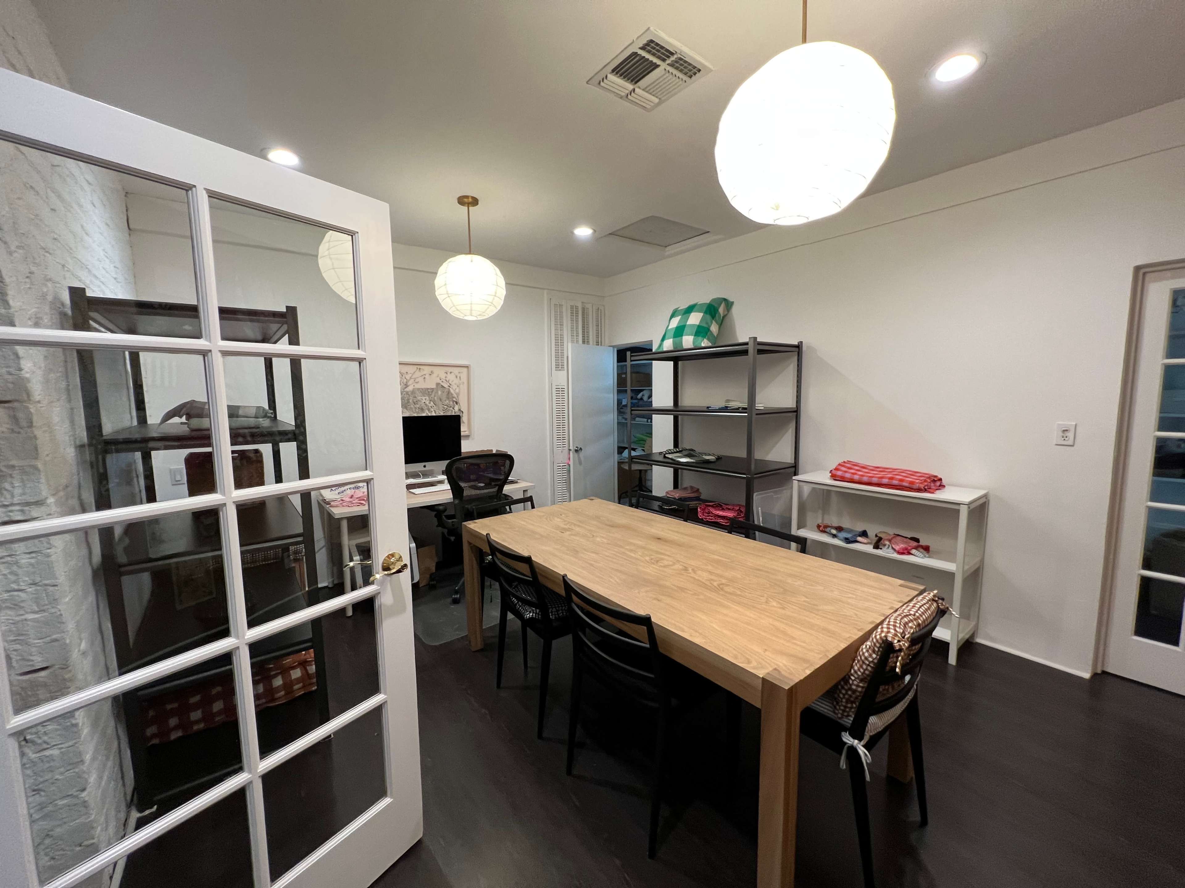 A spacious office features a long wooden table surrounded by black chairs, with shelves and a desk positioned against the walls.