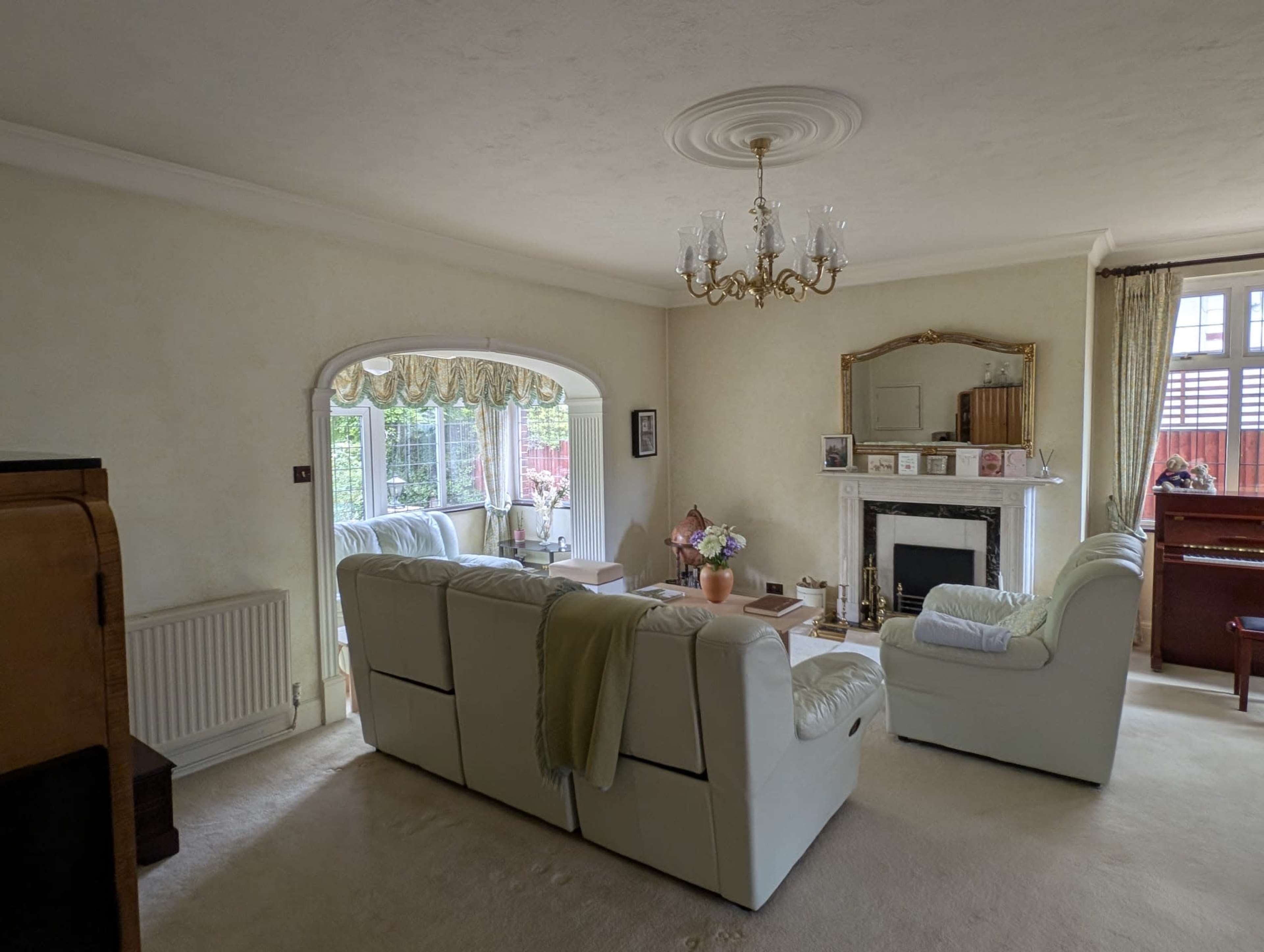 The living room features white leather sofas arranged around a coffee table, with a fireplace and large windows allowing natural light to fill the space.