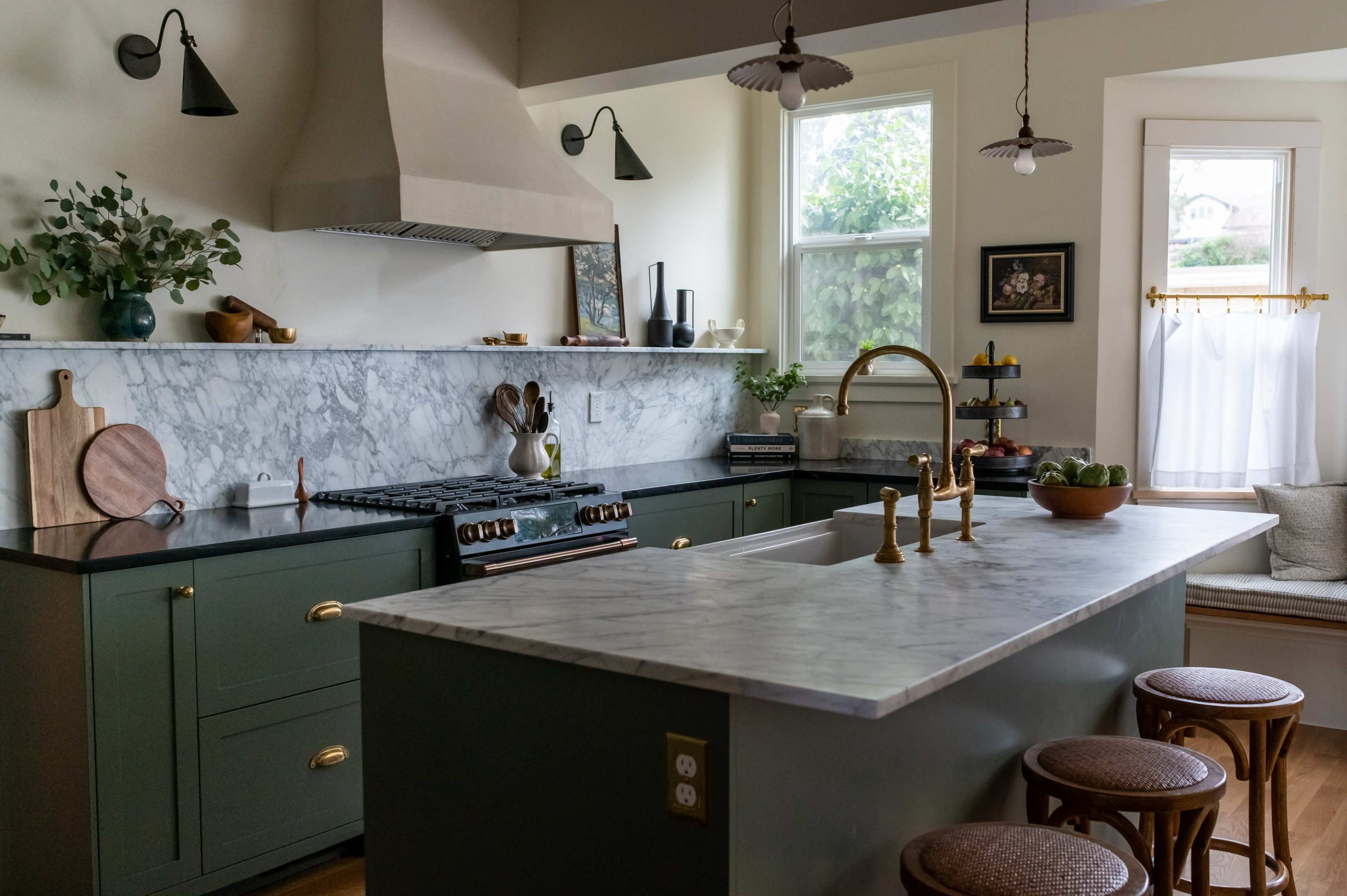 A modern kitchen features a marble countertop, dark green cabinetry, a gas stove, and natural light streaming through the windows.