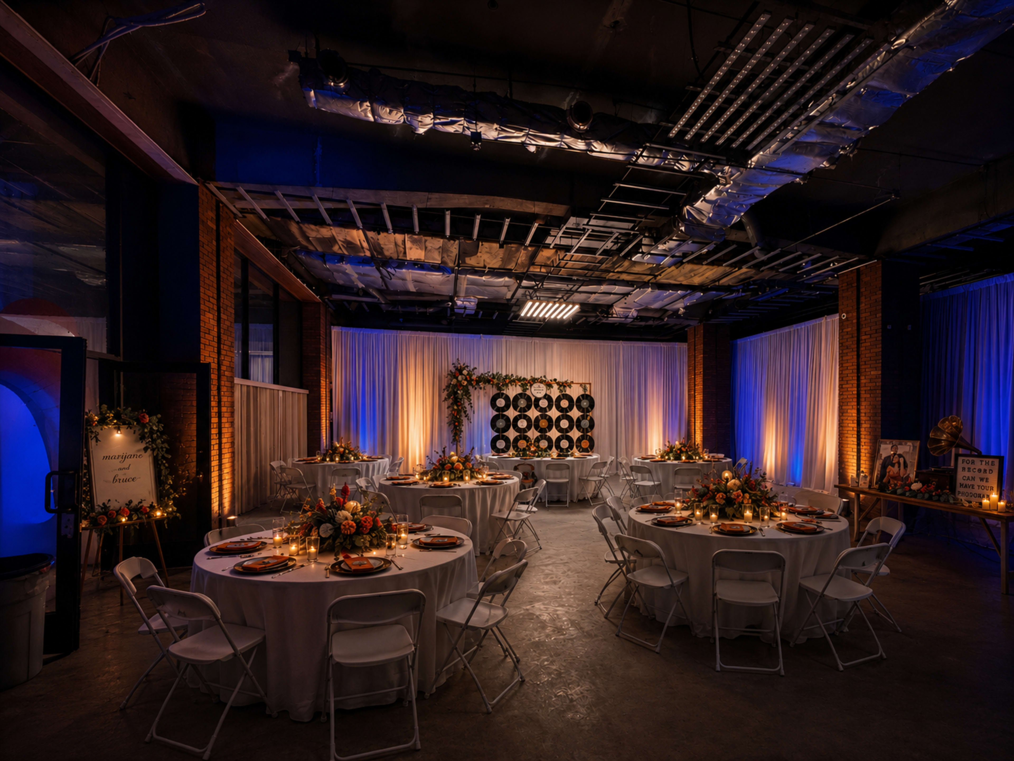 The image shows a decorated event space with round tables set for dining, featuring floral arrangements and illuminated backdrop elements.
