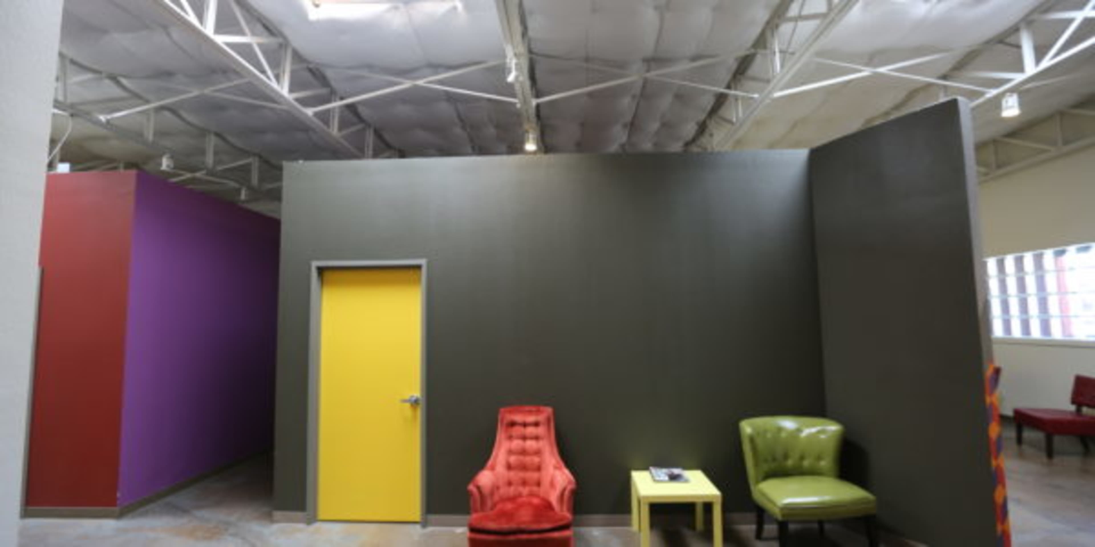 A spacious interior featuring a purple wall, a green wall, and two distinct seating areas with a red chair and a green chair beside a small yellow table.