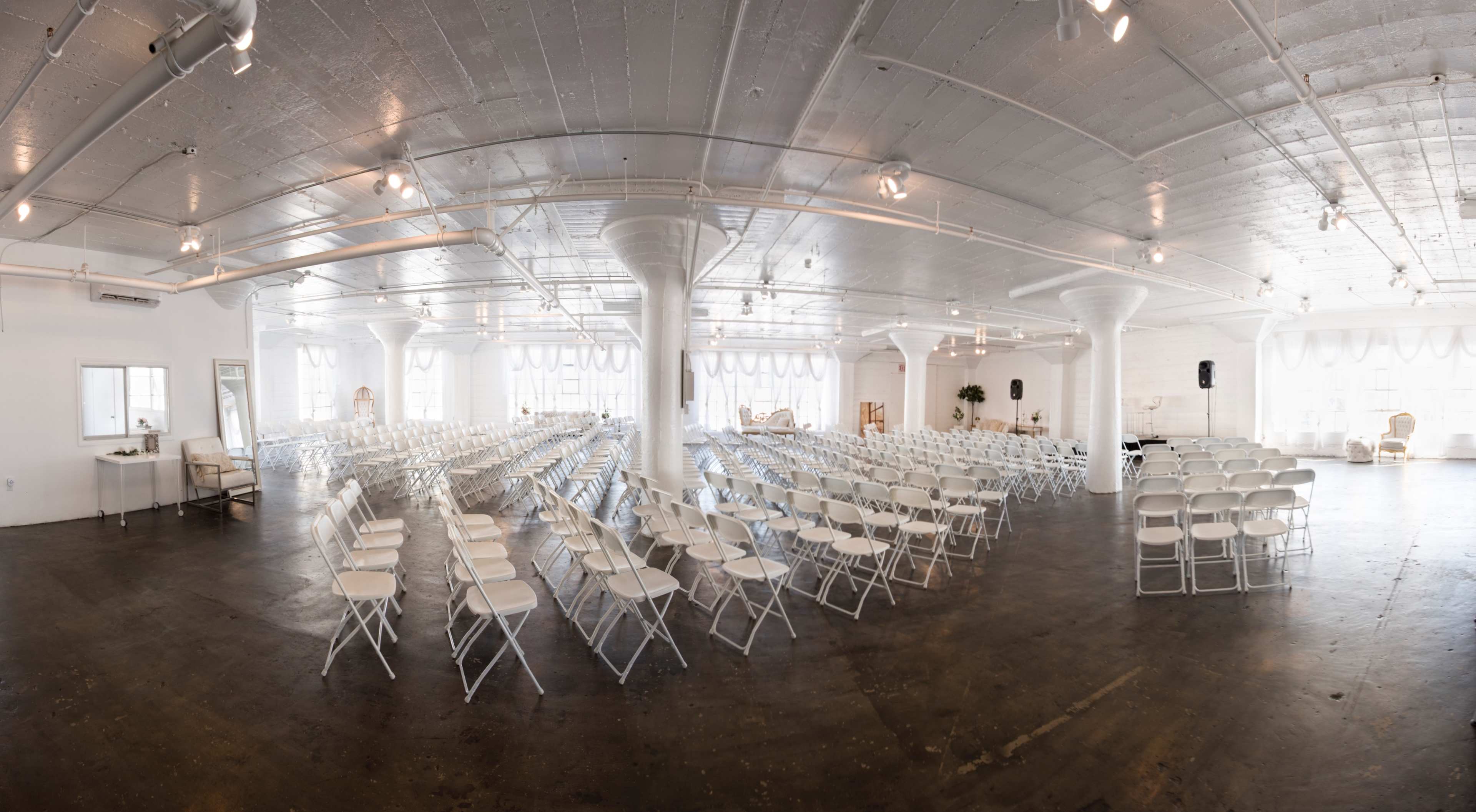 A spacious white event venue arranged with rows of white folding chairs for a gathering.