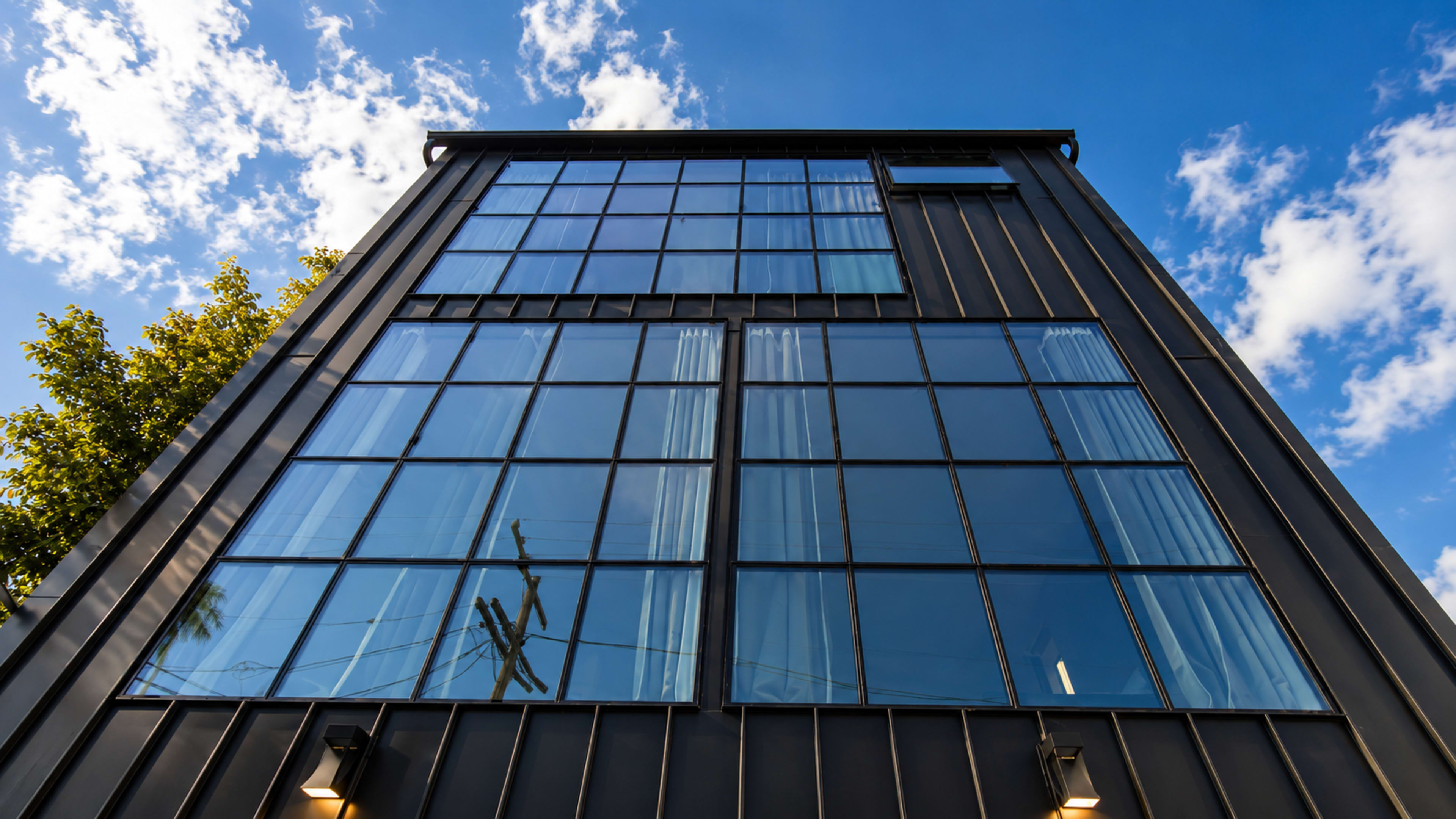 The image shows a modern building with a black metal facade and large glass windows reflecting the sky and surrounding trees.