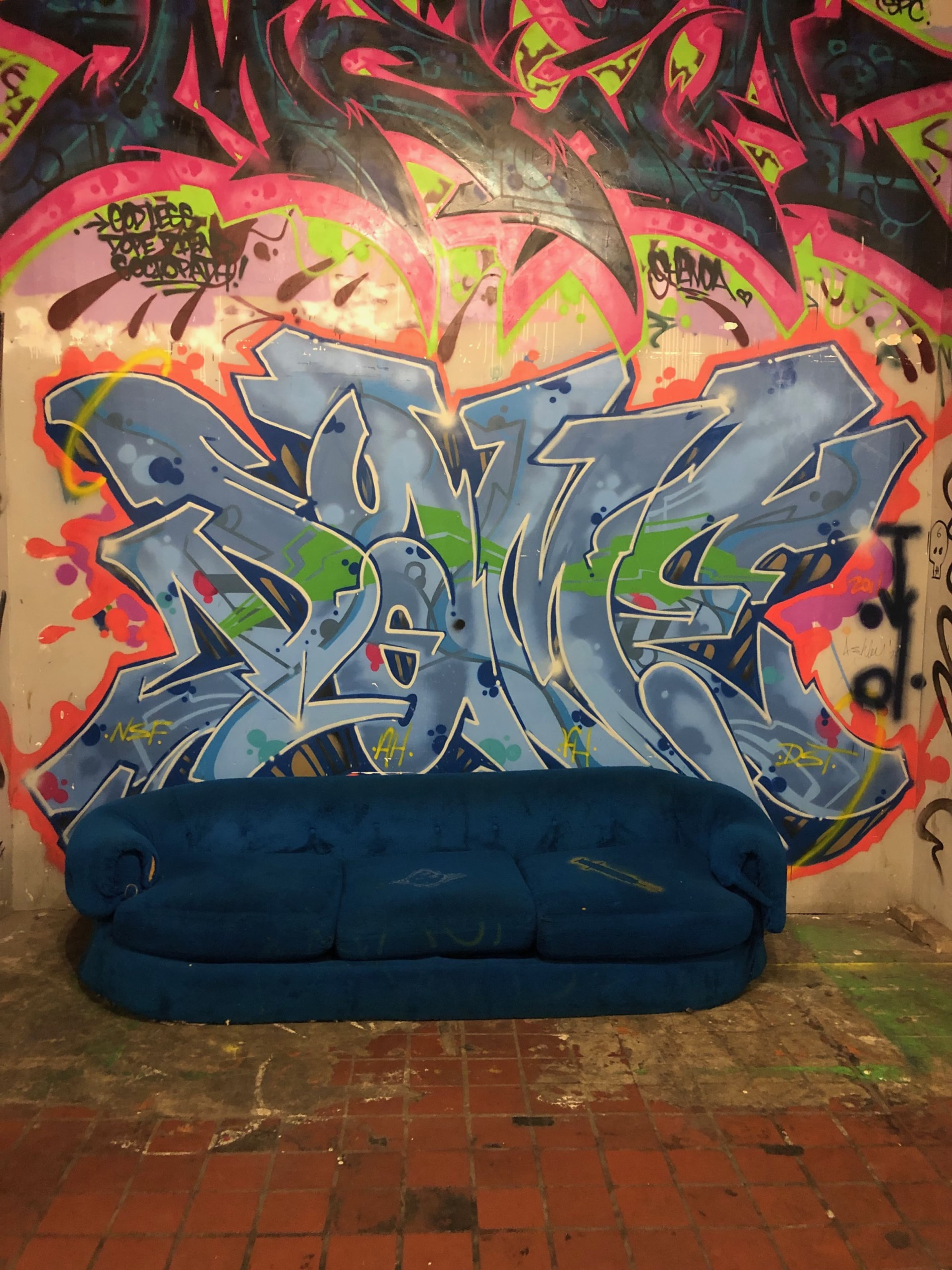 A blue couch is positioned in front of a vibrant graffiti wall featuring stylized lettering in various colors.