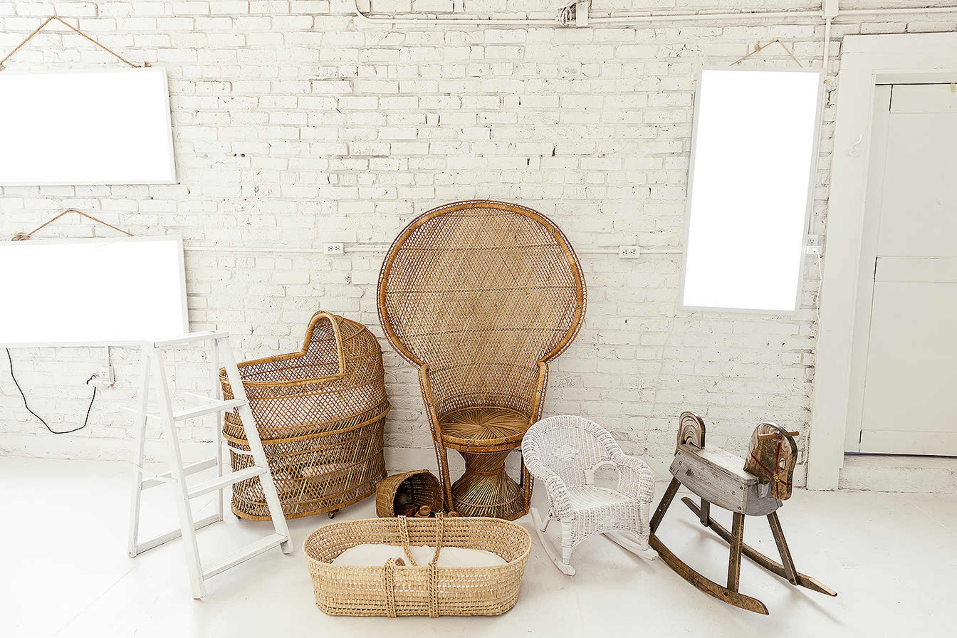 A collection of wicker chairs and a rocking horse placed against a white brick wall, with two blank frames hanging nearby.