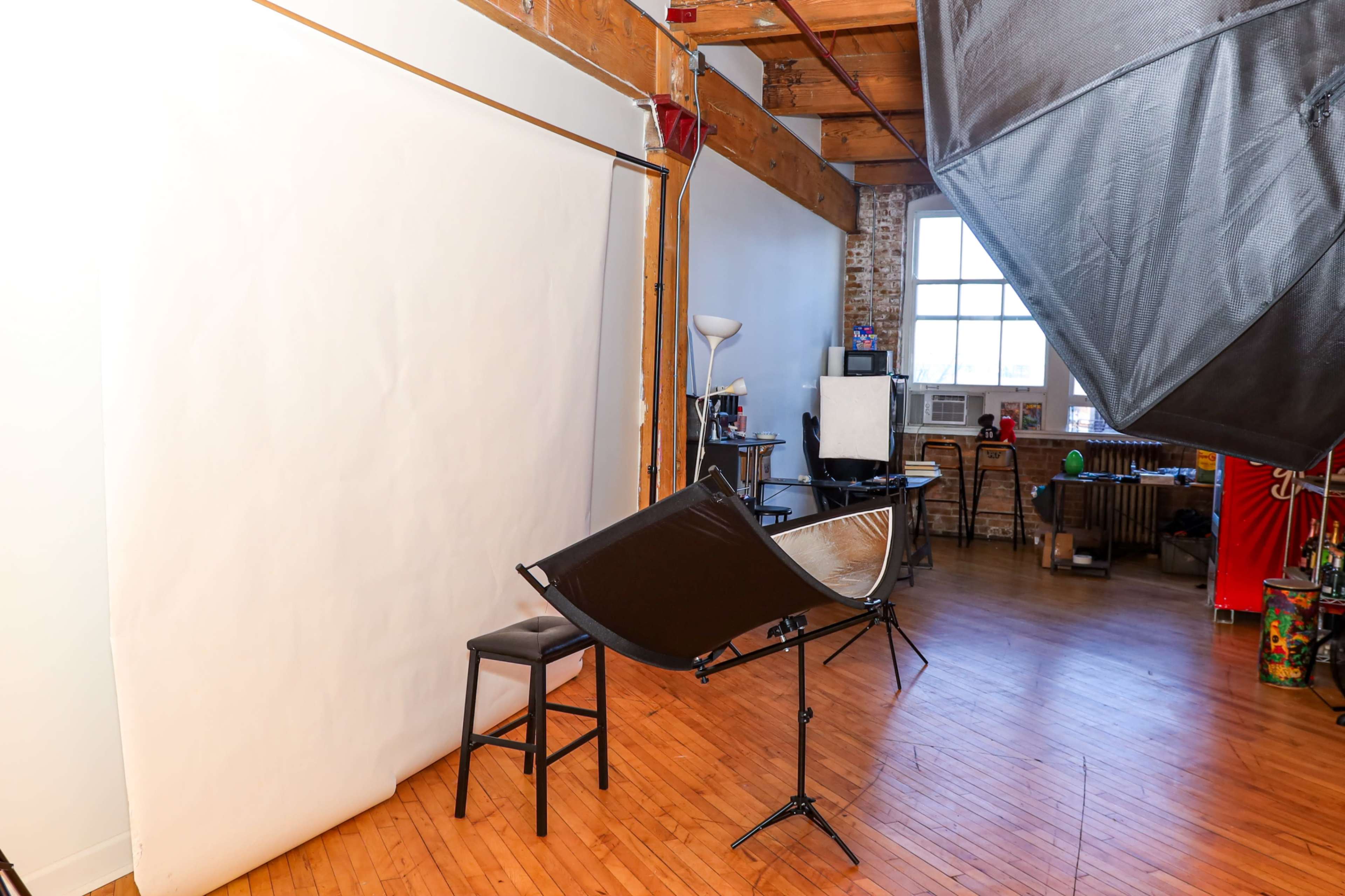 The image shows a photography studio with a white backdrop, a chair, and various lighting equipment set up for a shoot.