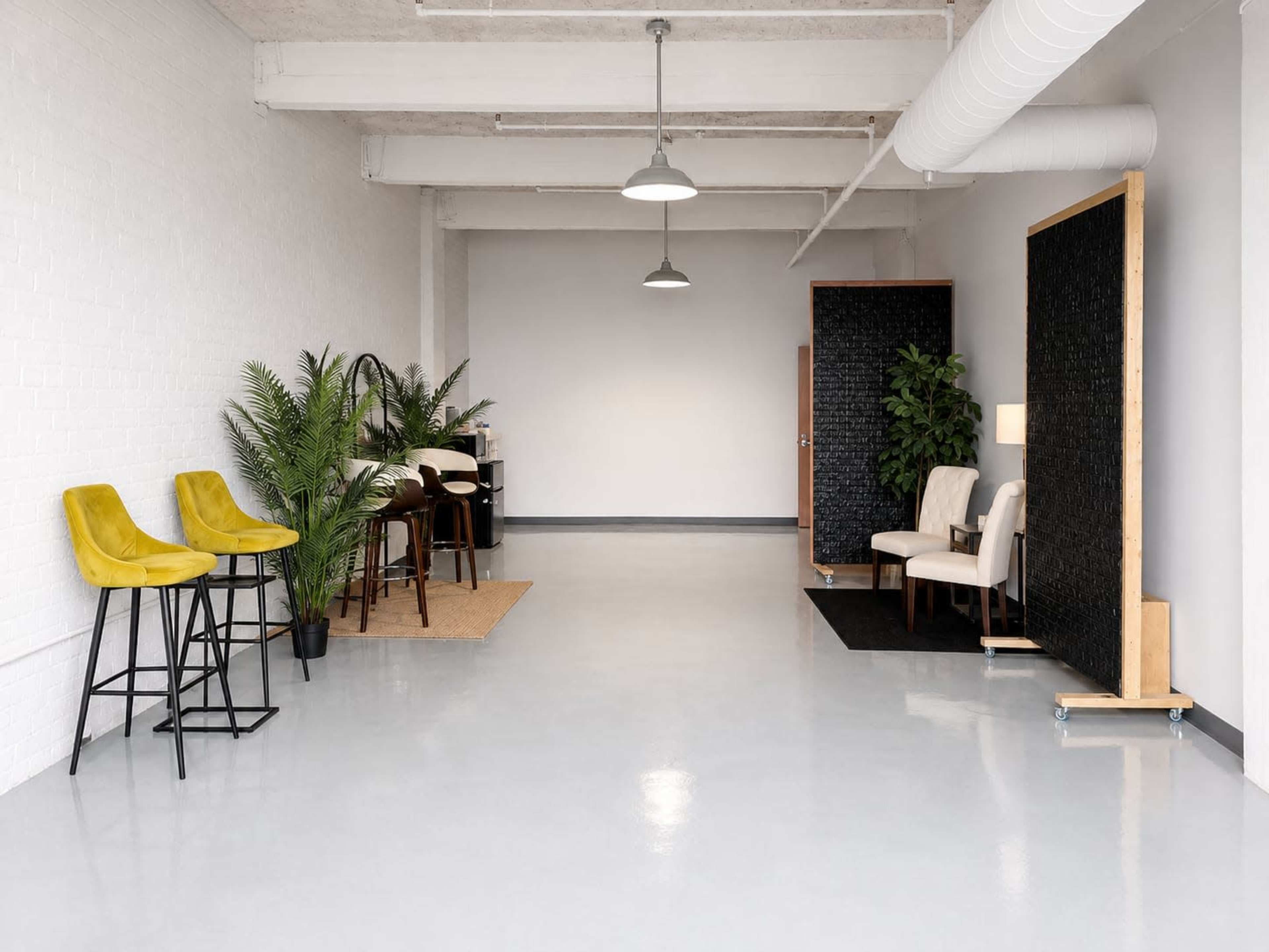 The image shows a minimalistic interior space featuring a few plants, seating arrangements, and modern furniture against a bright, neutral backdrop.