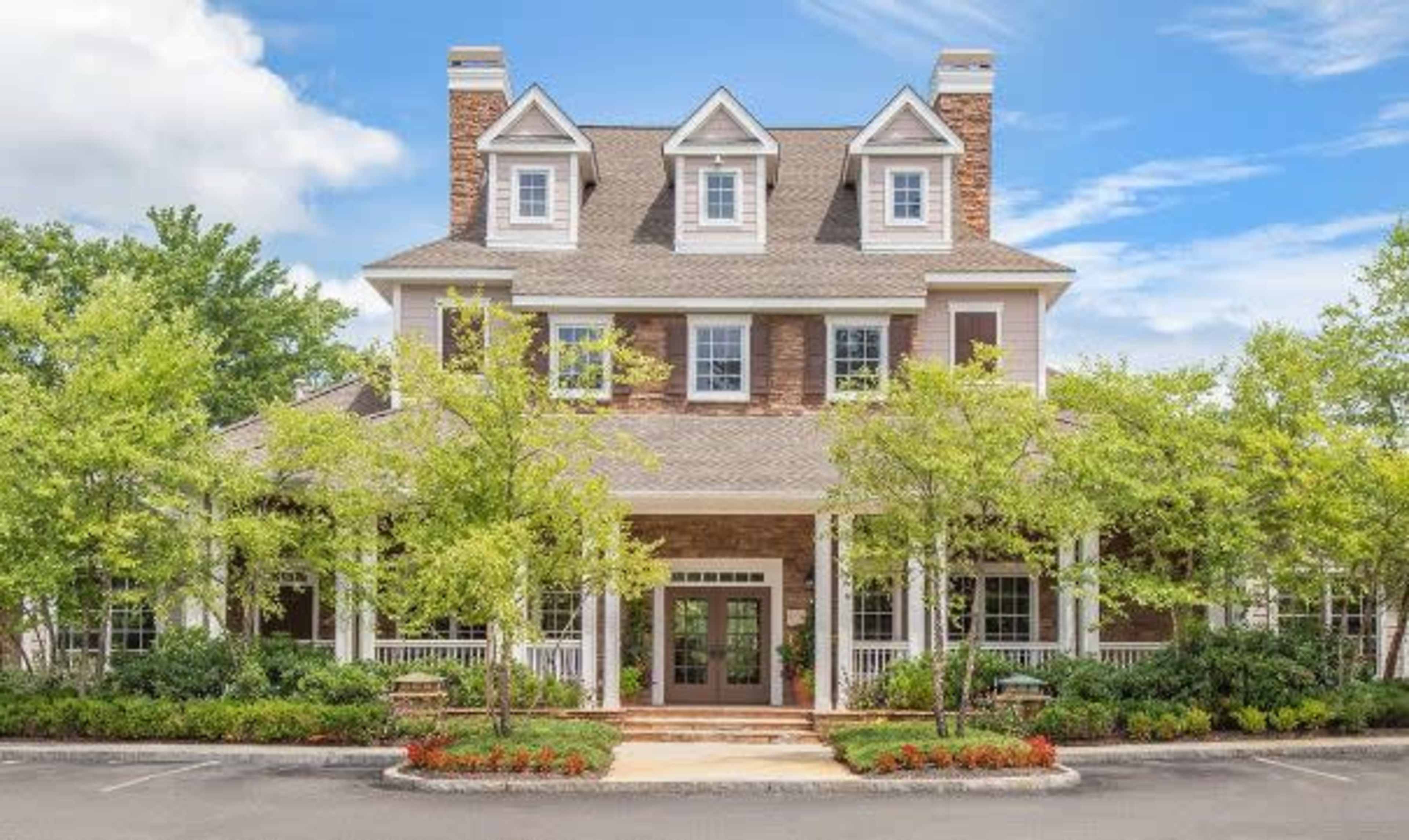 A three-story building with a stone and wood exterior is surrounded by landscaped greenery and benches.