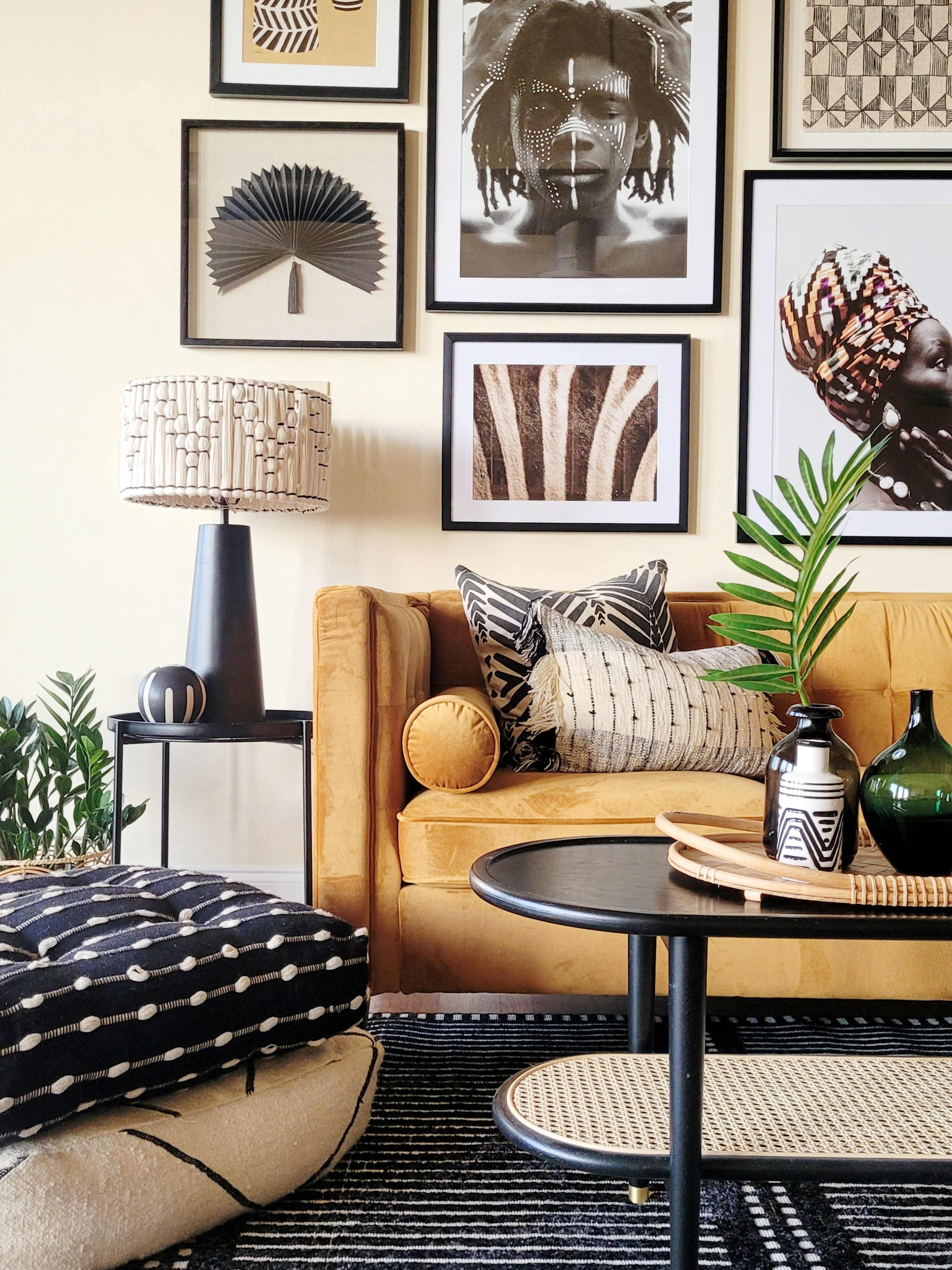 A stylish living room with a mustard yellow sofa adorned with patterned pillows, a coffee table, and an array of framed art on the wall.