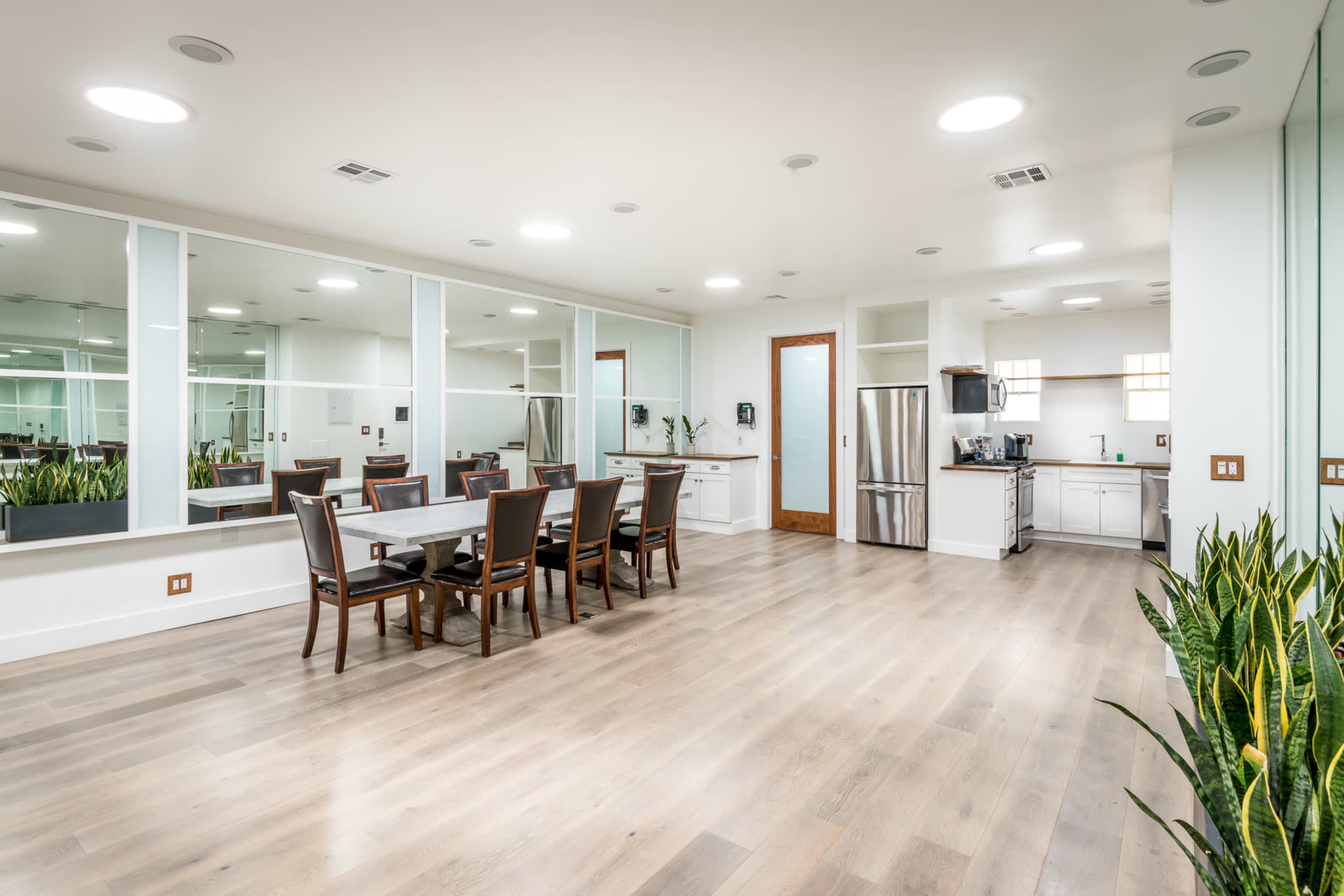A spacious dining area features a large table surrounded by chairs, with a kitchen visible in the background and large mirrors on one wall.