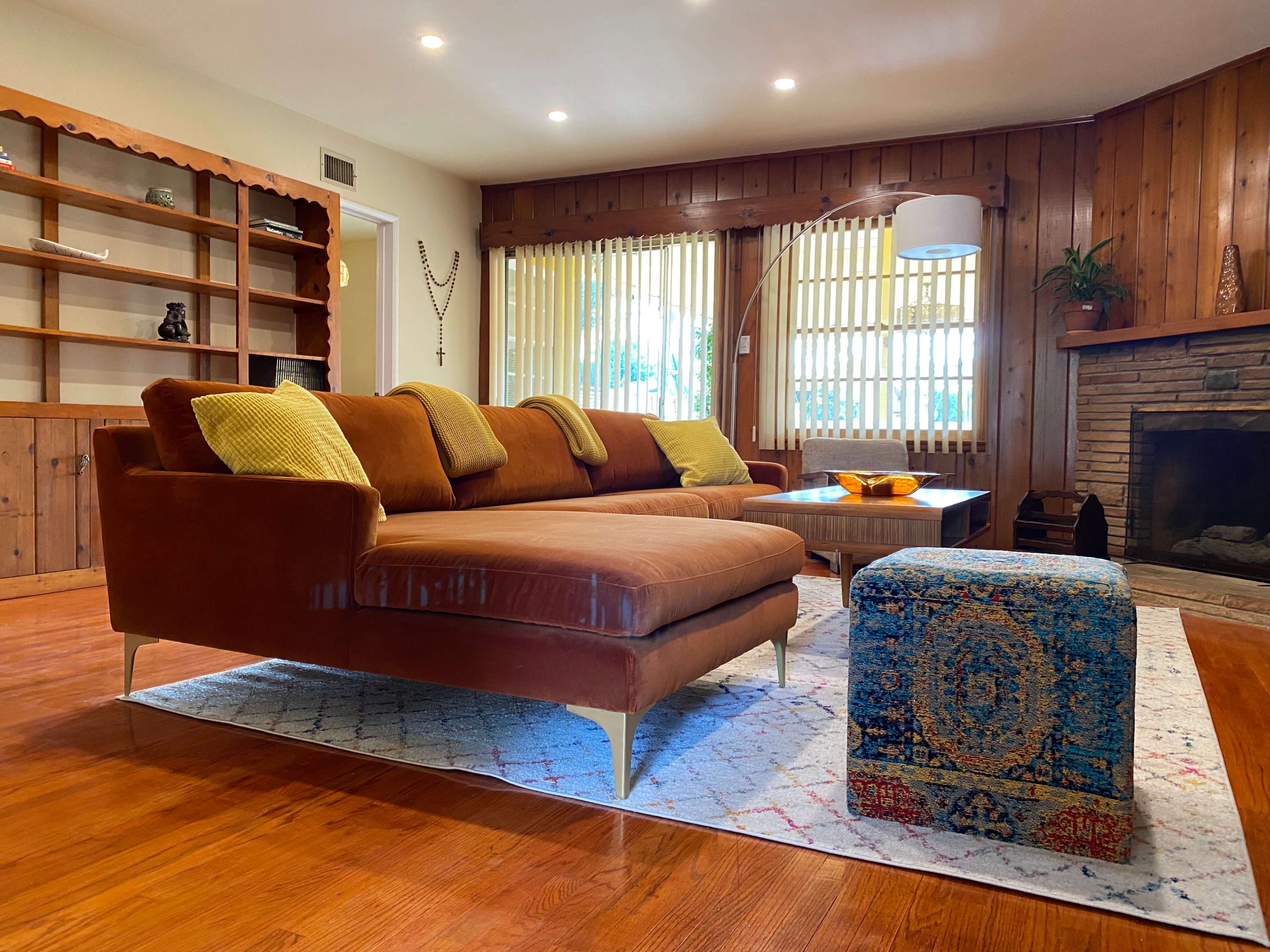 A cozy living room features a brown sectional sofa, a wooden bookshelf, and a stone fireplace.