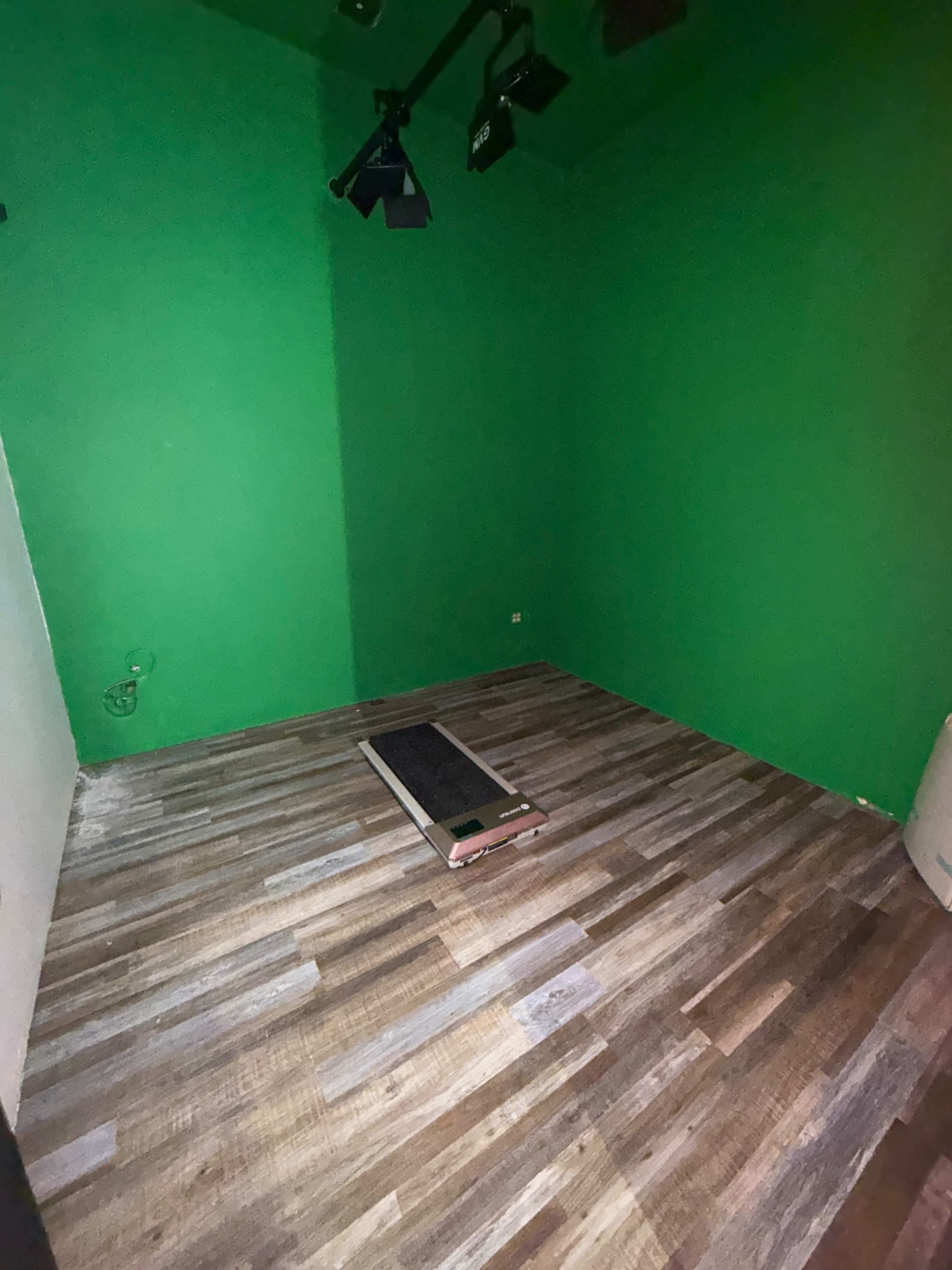 The image shows an empty room with green walls and a wooden floor, featuring a wooden platform in the center.