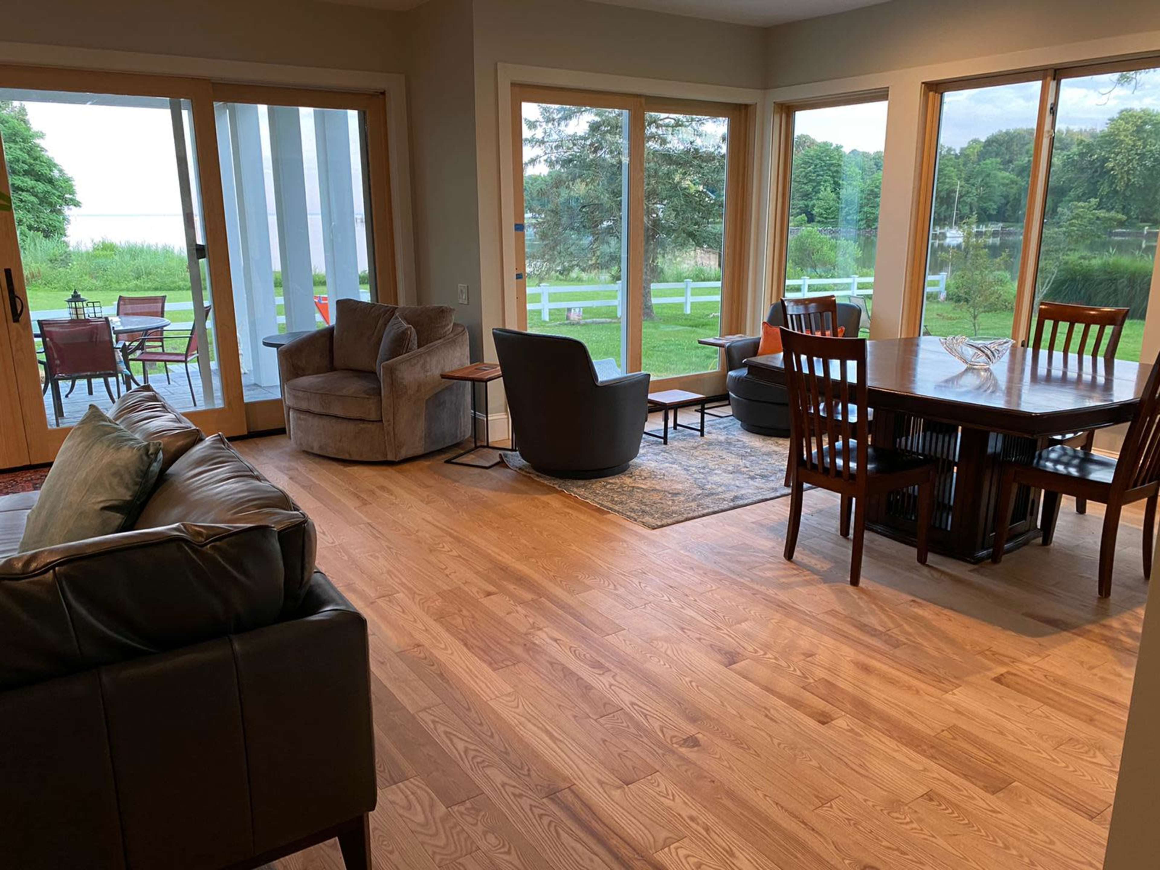 A living space with hardwood flooring, a dining area, and large windows overlooking a green outdoor landscape.