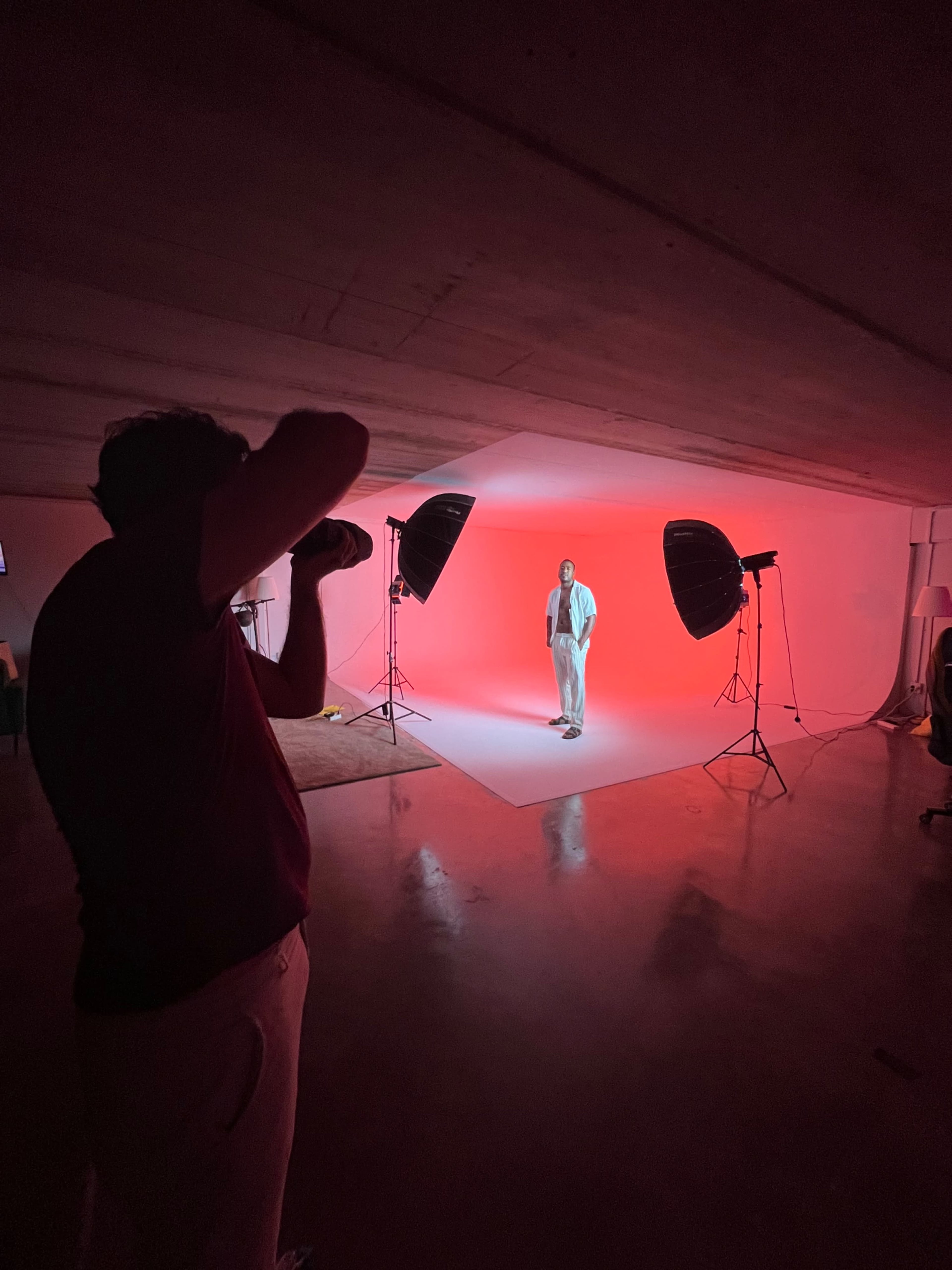 A photographer captures an individual posing under bright studio lights against a red backdrop.