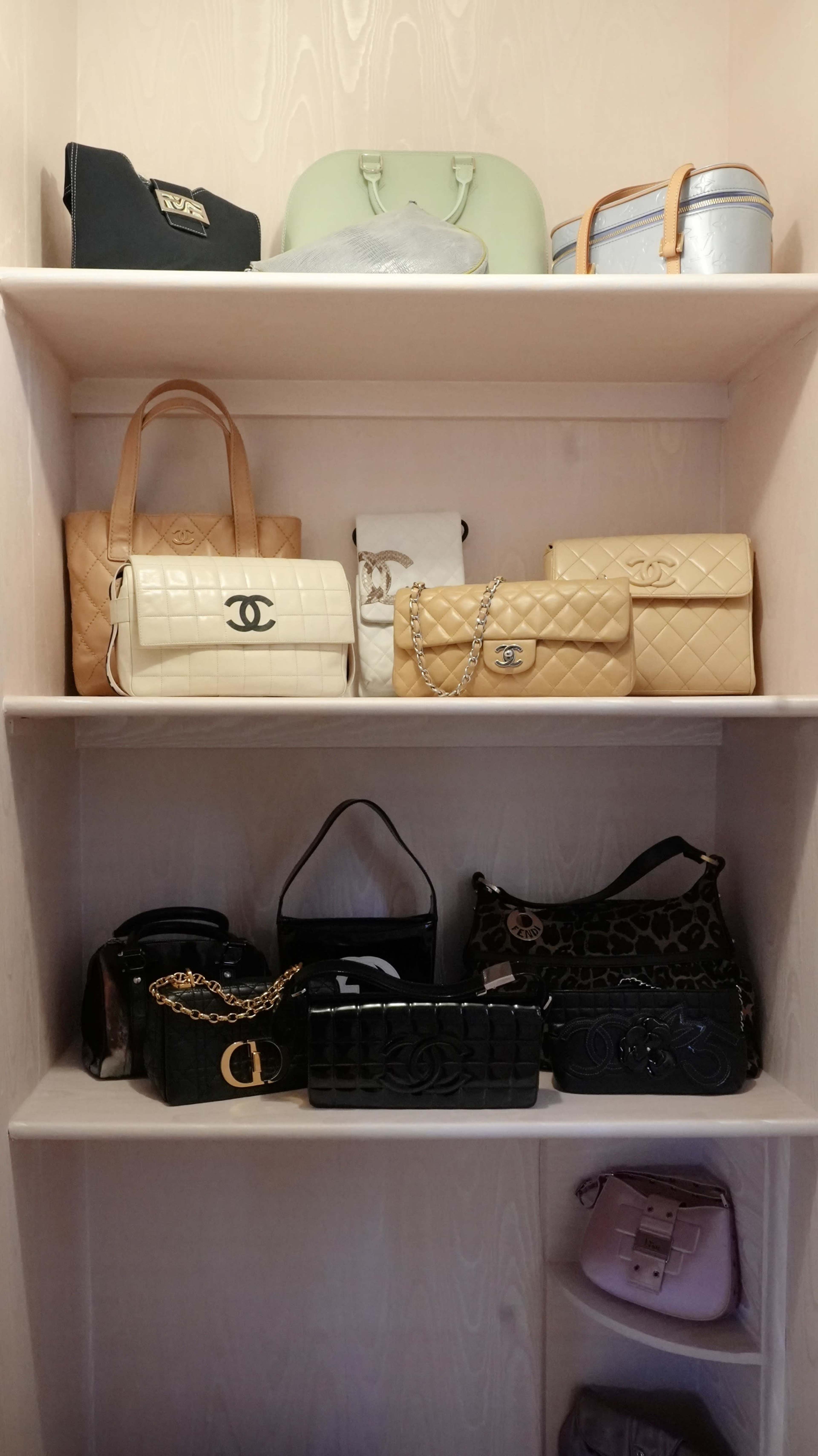A collection of various designer handbags is neatly arranged on white shelves in a closet.