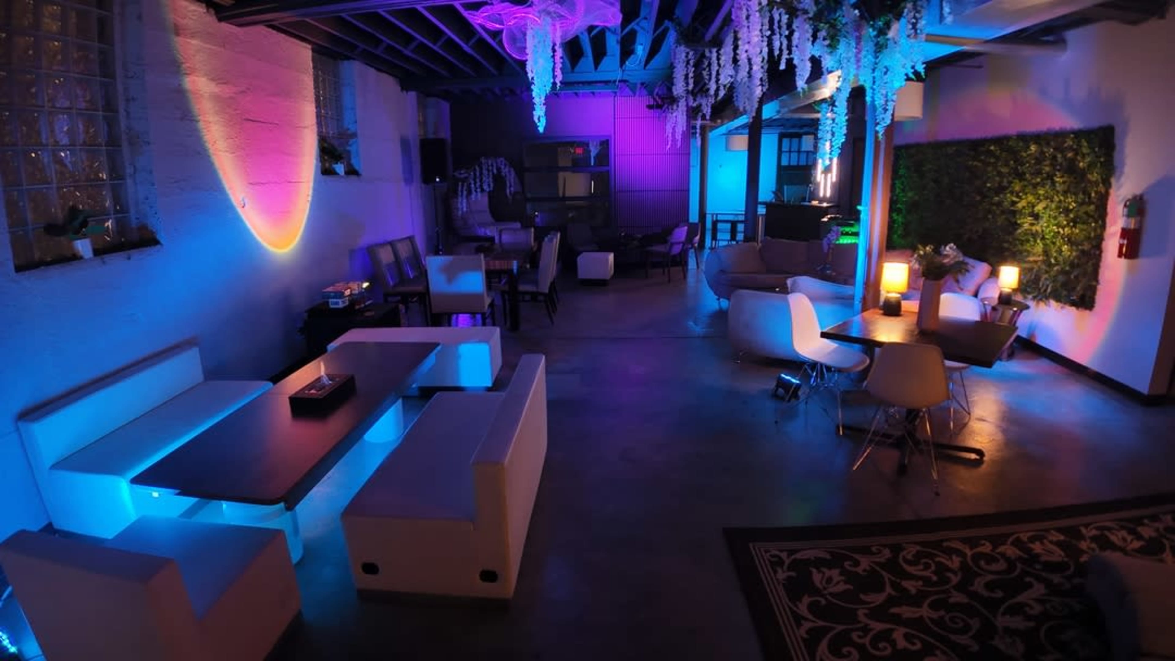The image shows a modern lounge space with various seating arrangements illuminated by colorful LED lights.