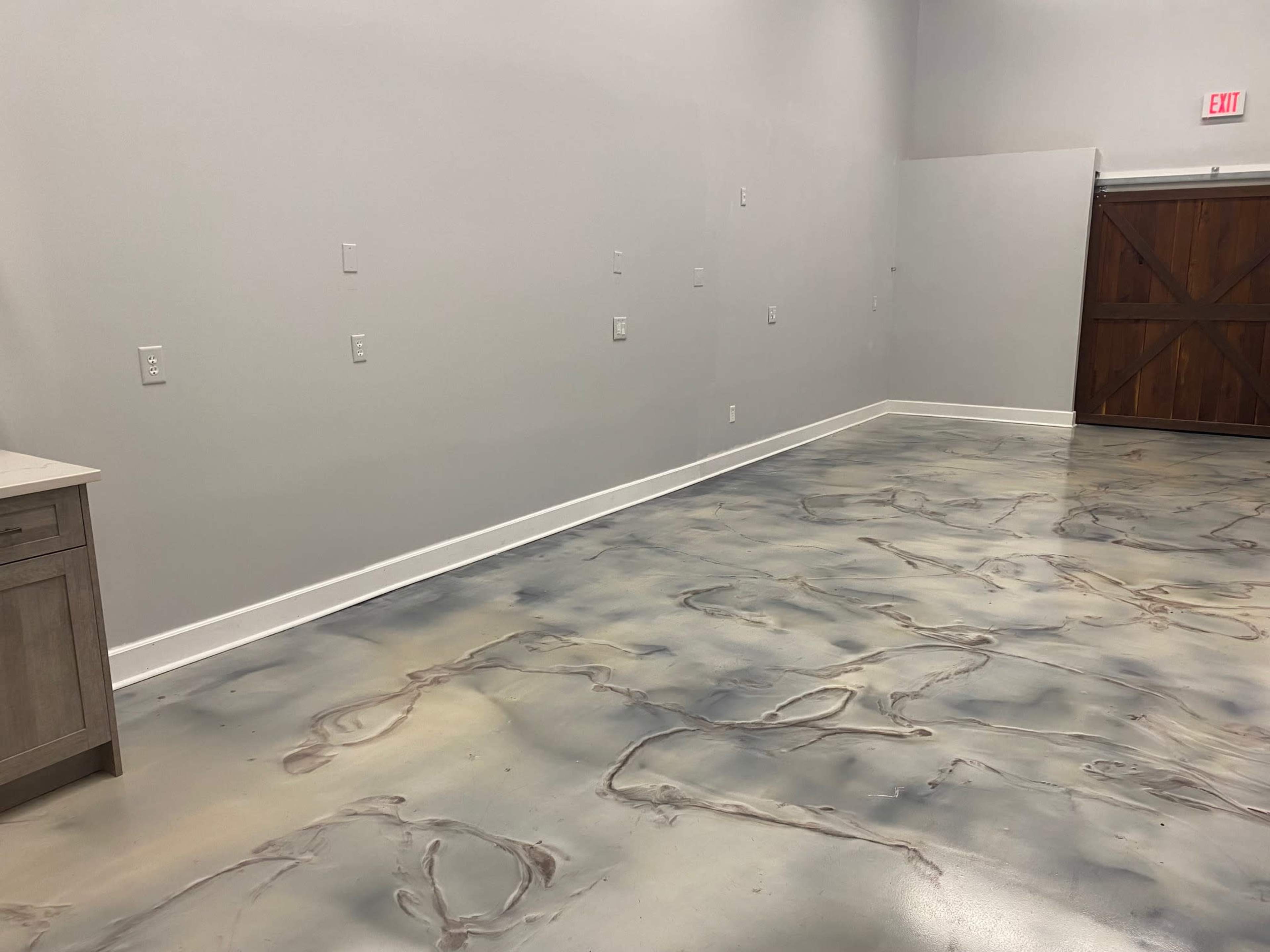 An empty room with a polished, patterned concrete floor and a wooden double door at one end.
