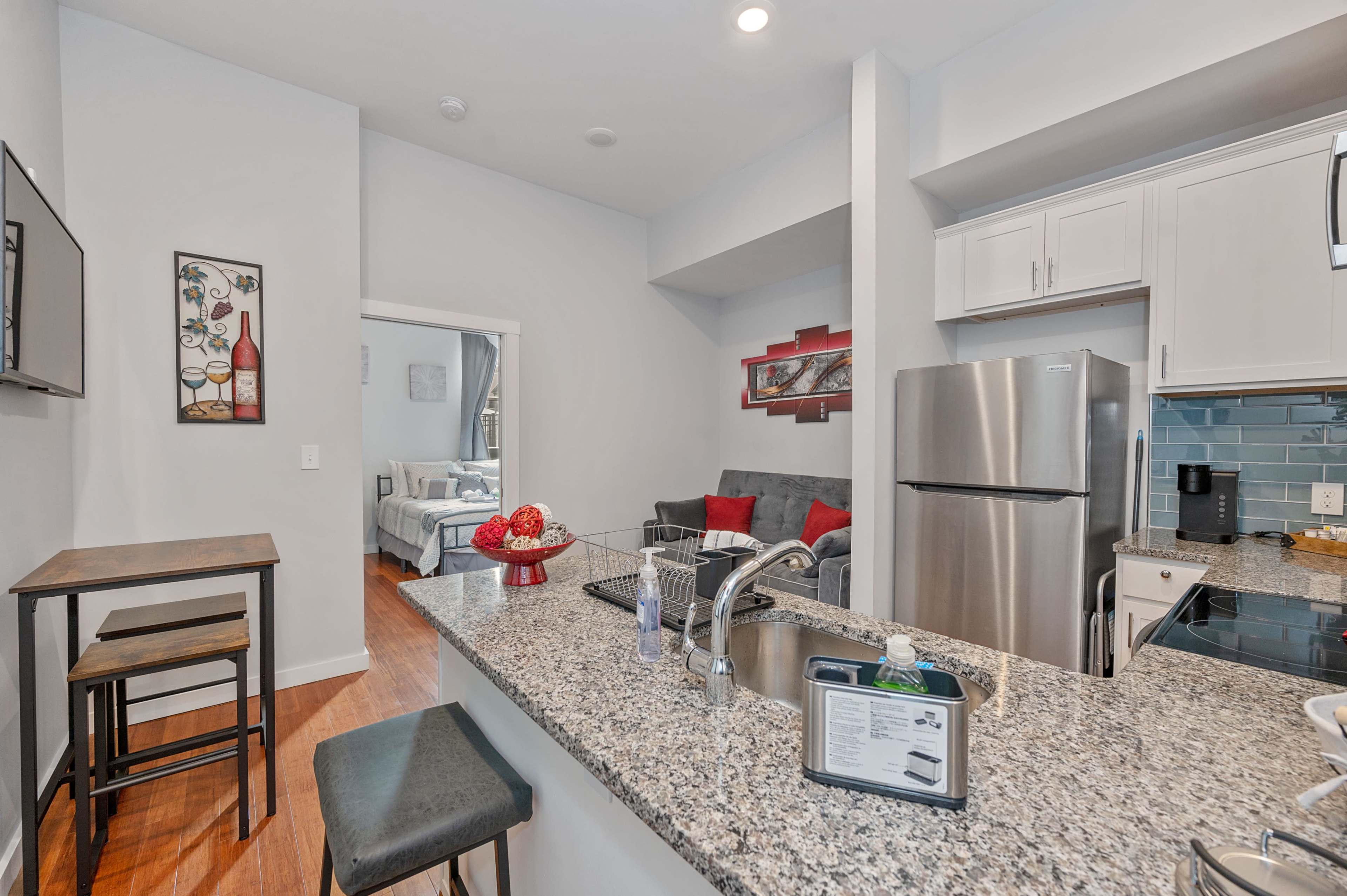 A modern kitchen with a granite countertop, stainless steel appliances, and a view into a living area with a couch and decor.