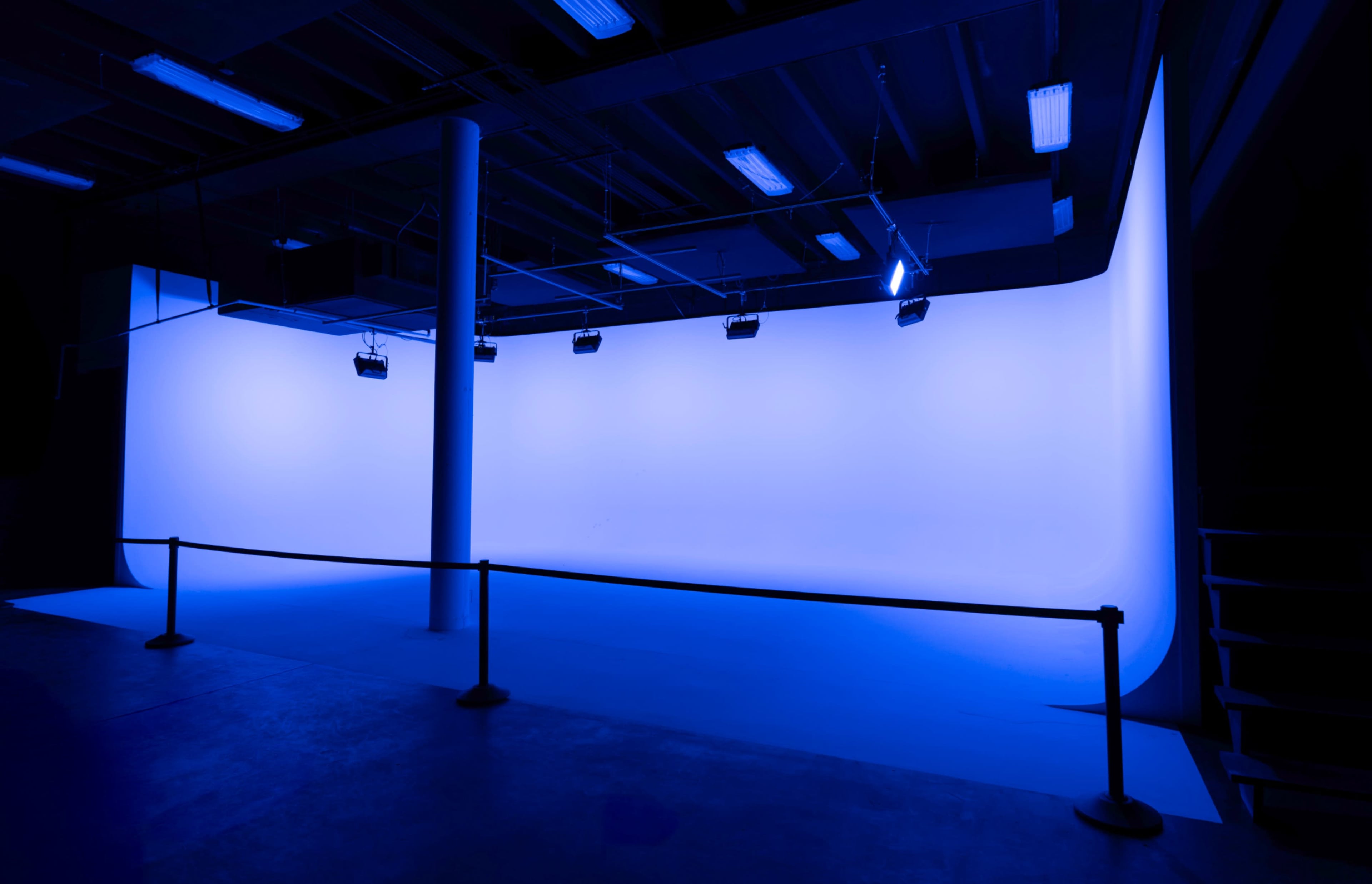 The image shows a spacious studio with a blue backdrop, illuminated by overhead lights.