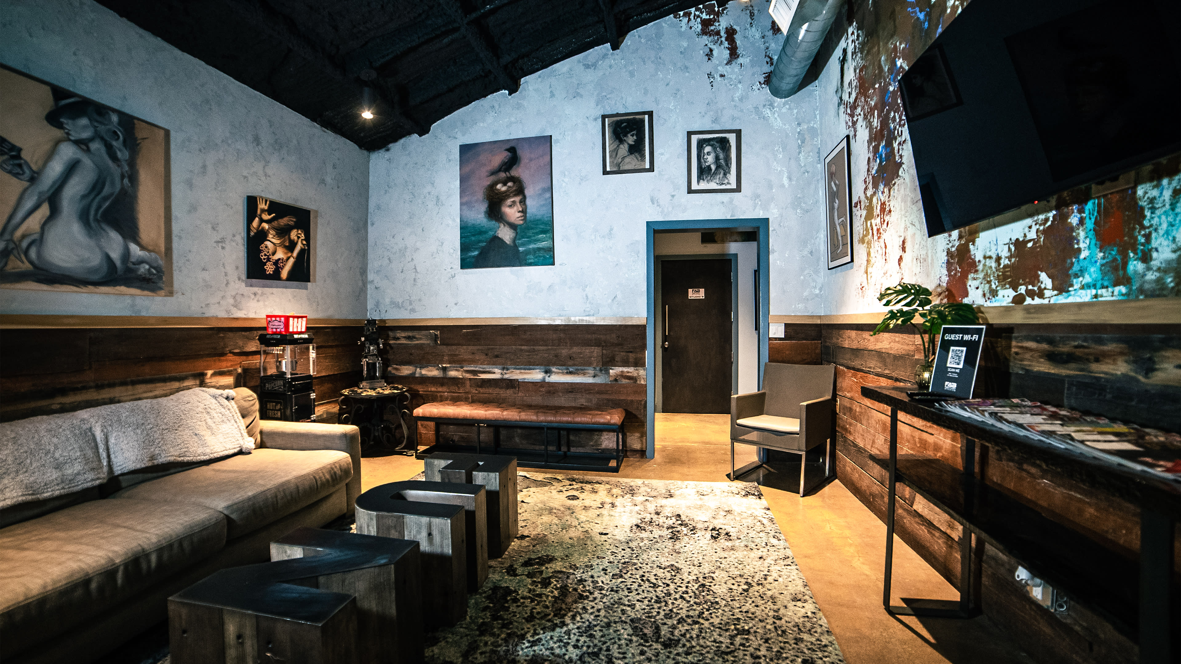 A cozy lounge area with a sectional couch, wooden accents, and several artworks on the walls.