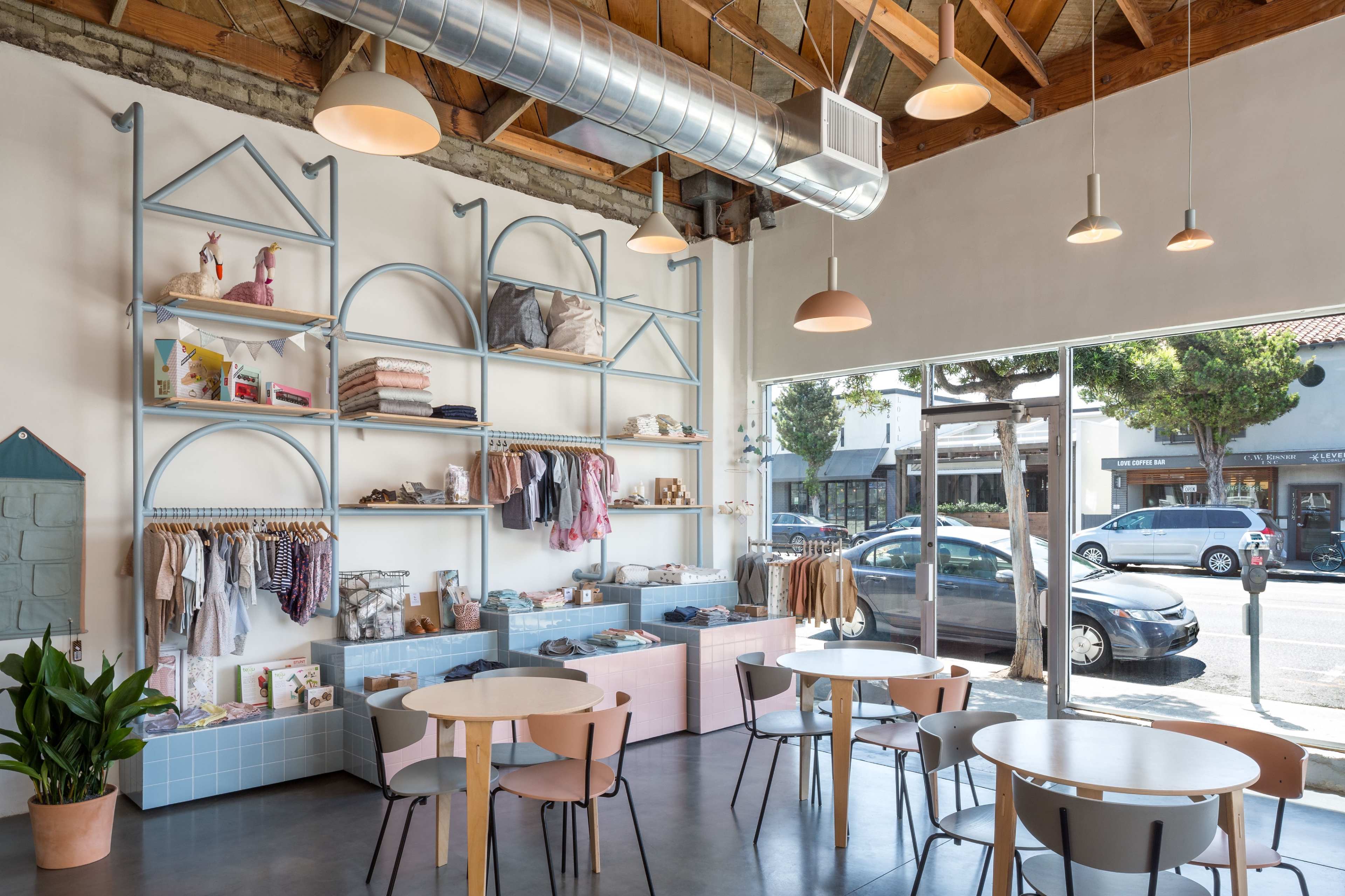 A modern retail space features colorful shelving displaying clothing and accessories, with circular tables and chairs arranged for customer seating.